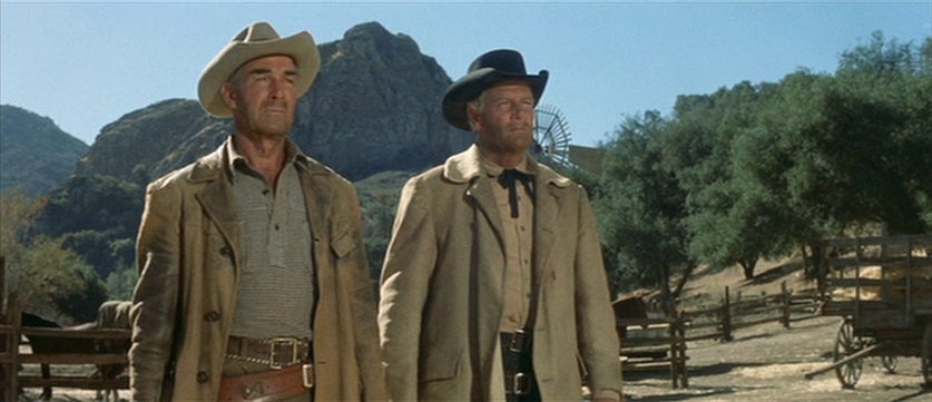 Randolph Scott and Joel McCrea as old Westerners on a farm at the foot of the mountains, with routinely worn looks full of firm determination.