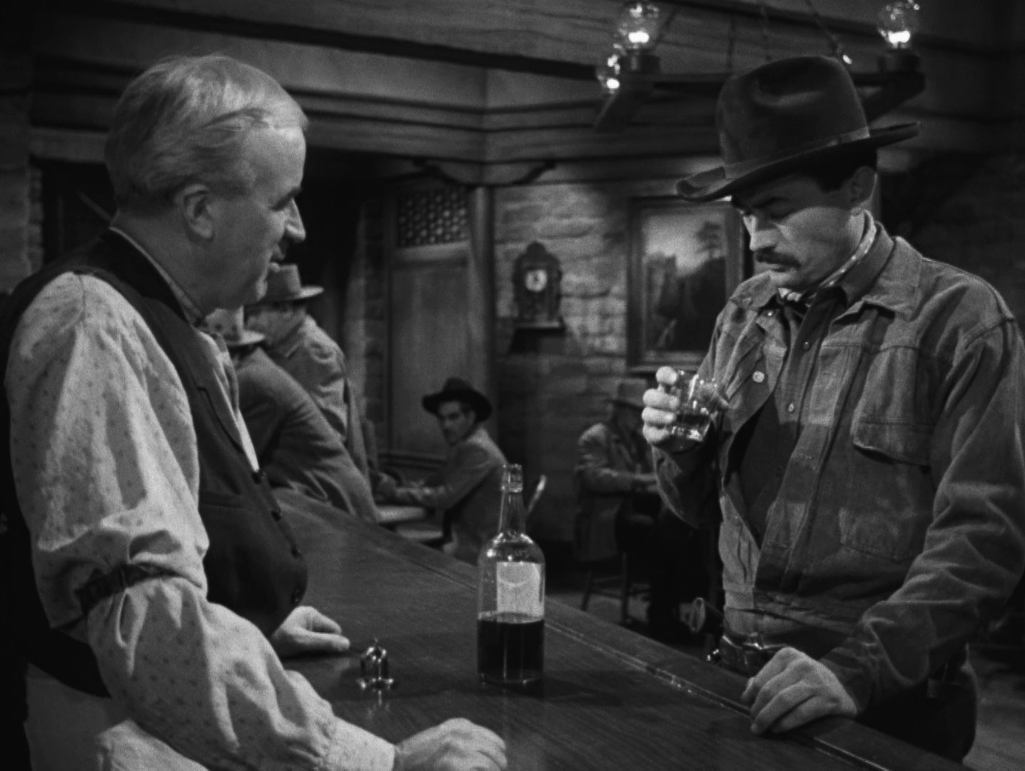 Schwarz-Weiß-Szene: Gregory Peck als Jimmy Ringo, der an der Theke eines Saloons im Beisein des Barkeepers in ein Whiskeyglas starrt, vor ihm auf den Tresen steht eine halbvolle Flasche.