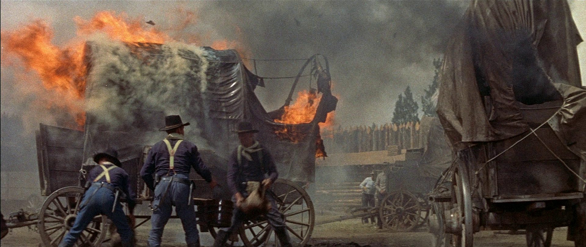 Drei Kavalleristen vor einem brennenden Planwagen in einem Fort.