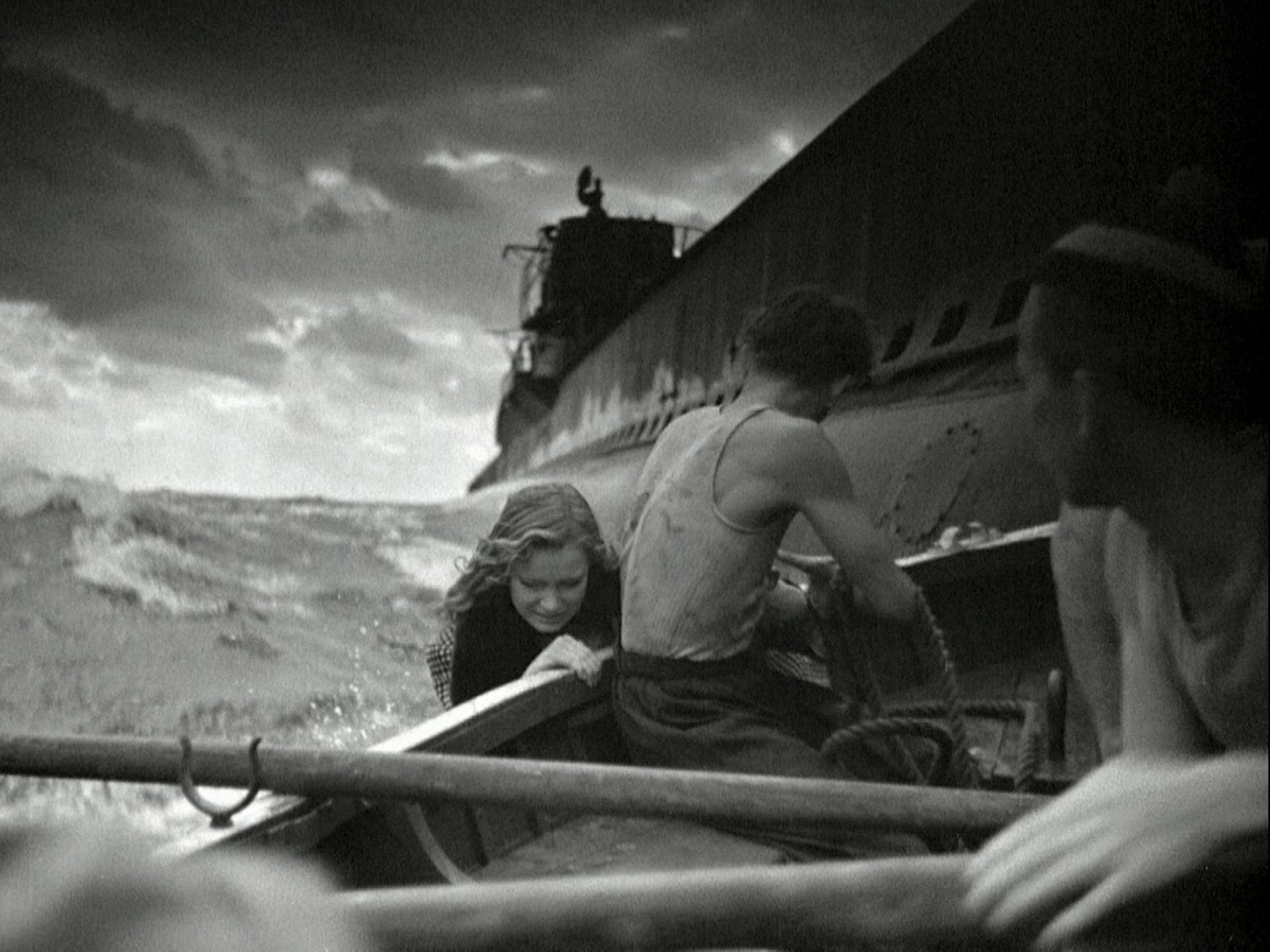 Two sailors in rough waters in a rowing boat to which a young woman is clinging, with a submarine in the background.