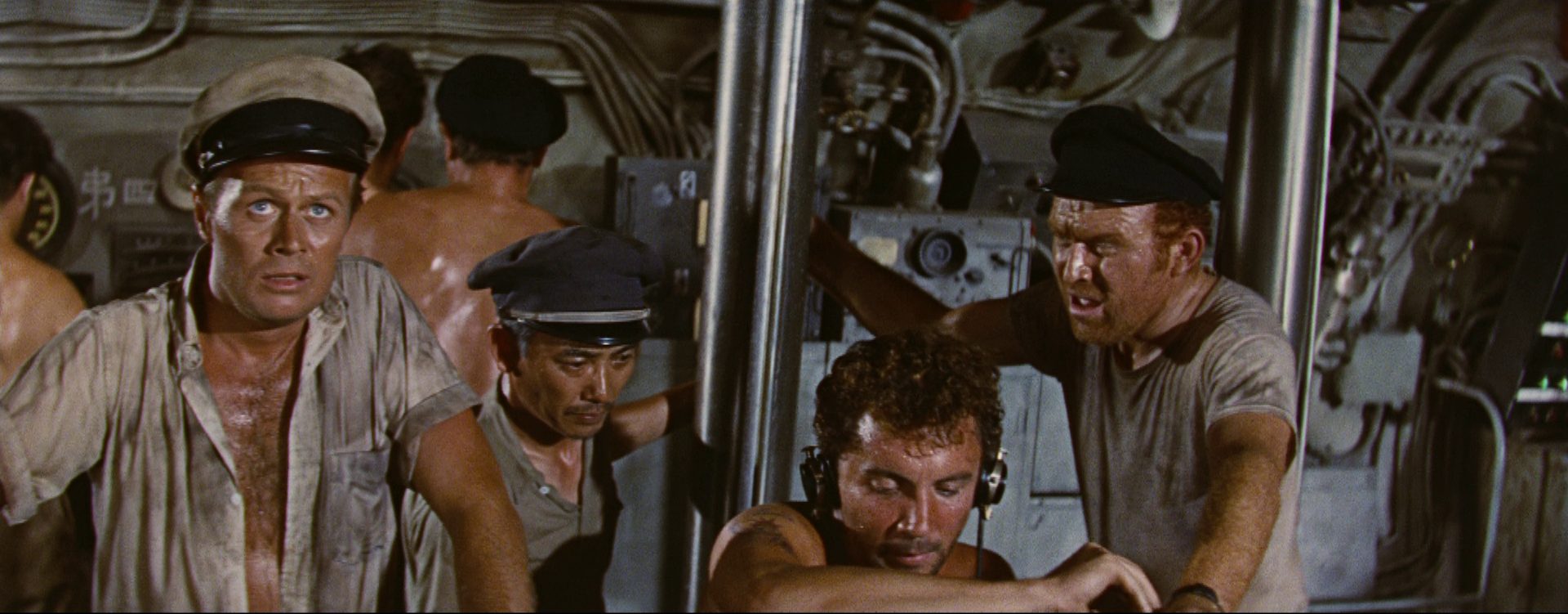 Richard Widmark as commander in the presence of some crew members in a sweaty atmosphere in the submarine.