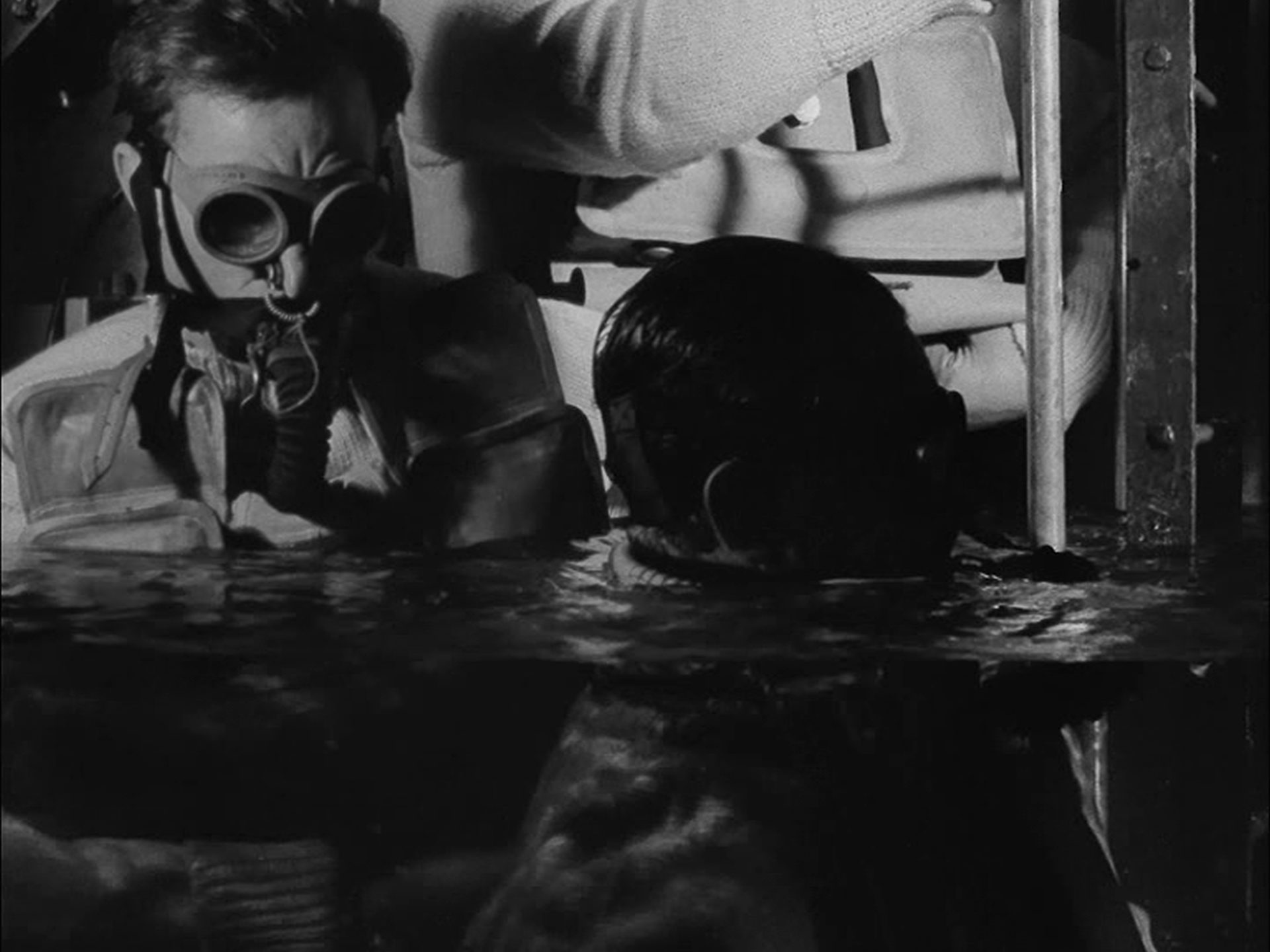 Oppressive shot of two seamen with diving rescuers on in a half-flooded exit chamber.