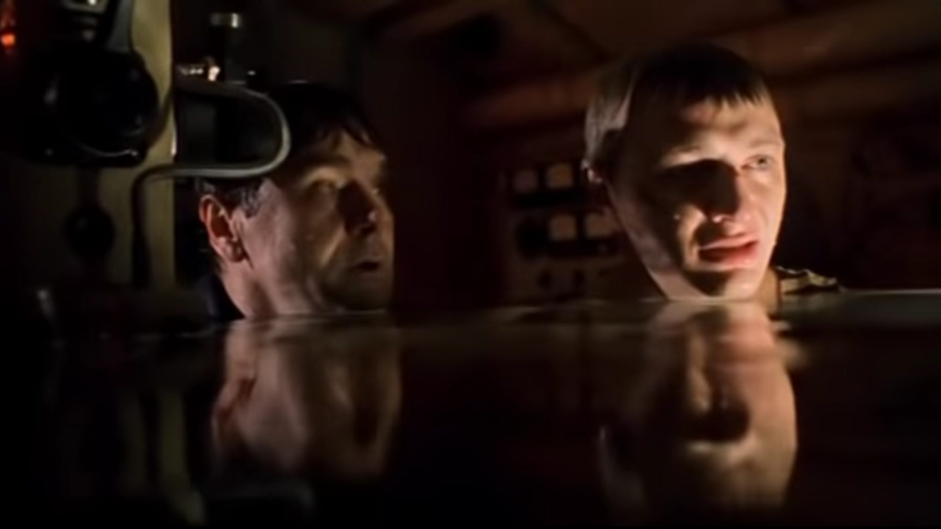 Close-up of two sailors with their heads sticking out of the water in the flooded submarine in dim light.