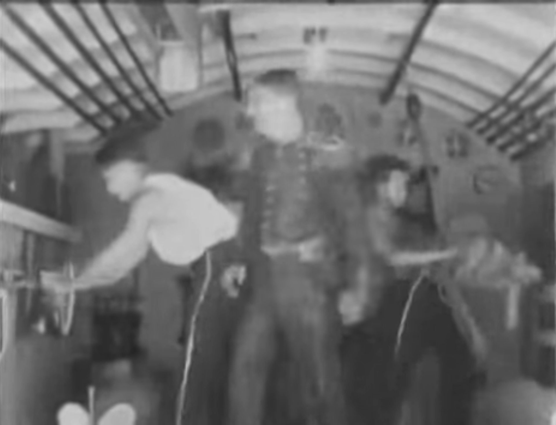 Kommandant im U-Boot-Innern, zu beiden Seiten neben ihm je ein Seemann bei der Arbeit.