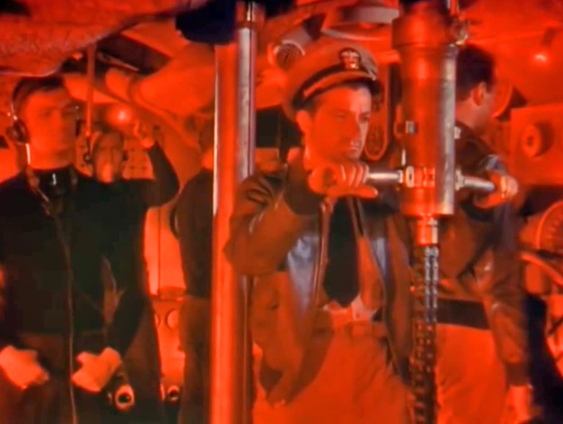 Dana Andrews als U-Boot-Kommandant beim konzentrierten Blick durch das Periskop im Rotlicht, mehrere Seeleute auf Station.