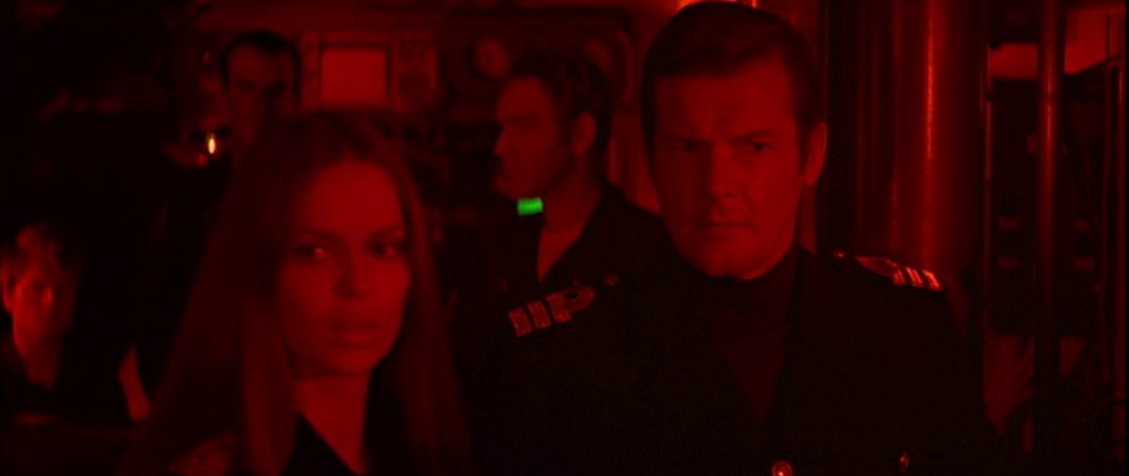 Barbara Bach und Roger Moore als Spione mit besorgten Gesichtern im Rotlicht der Kommandozentrale eines U-Bootes.