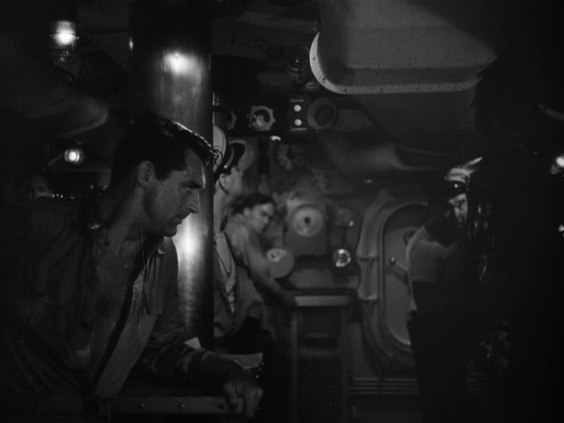 Sinister black and white scene with a young Cary Grant in the foreground with his shirt open and eyes strained inside a submarine.