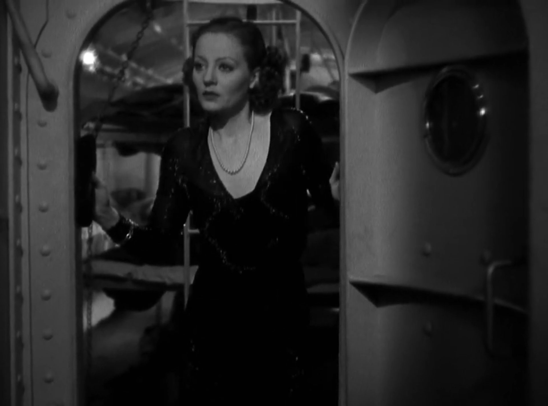Schwarz-Weiß-Szene mit Tallulah Bankhead im Abendkleid und mit suchendem Blick im Schott eines U-Bootes, im Hintergrund Kojen.