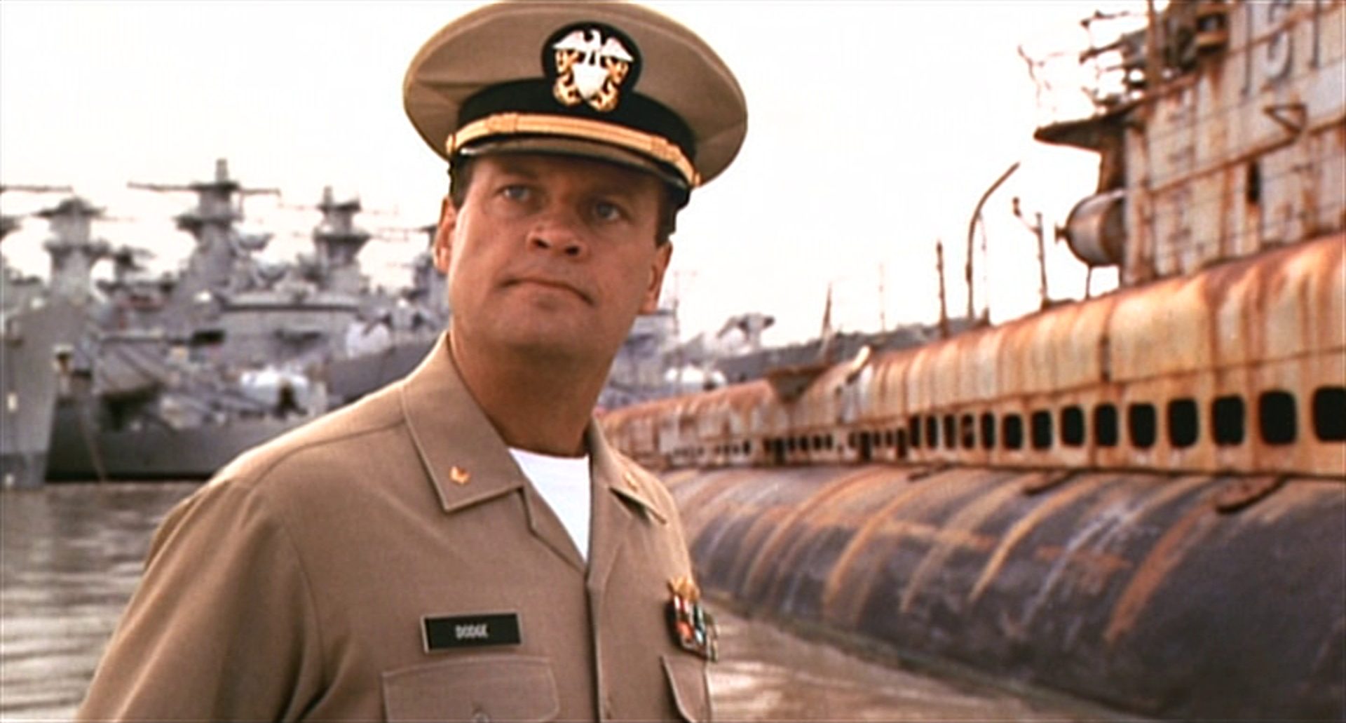 Kelsey Grammer im Hafen als U-Boot-Kommandant mit entschieden empörtem Blick, im Hintergrund ein U-Boot in desolatem Zustand.