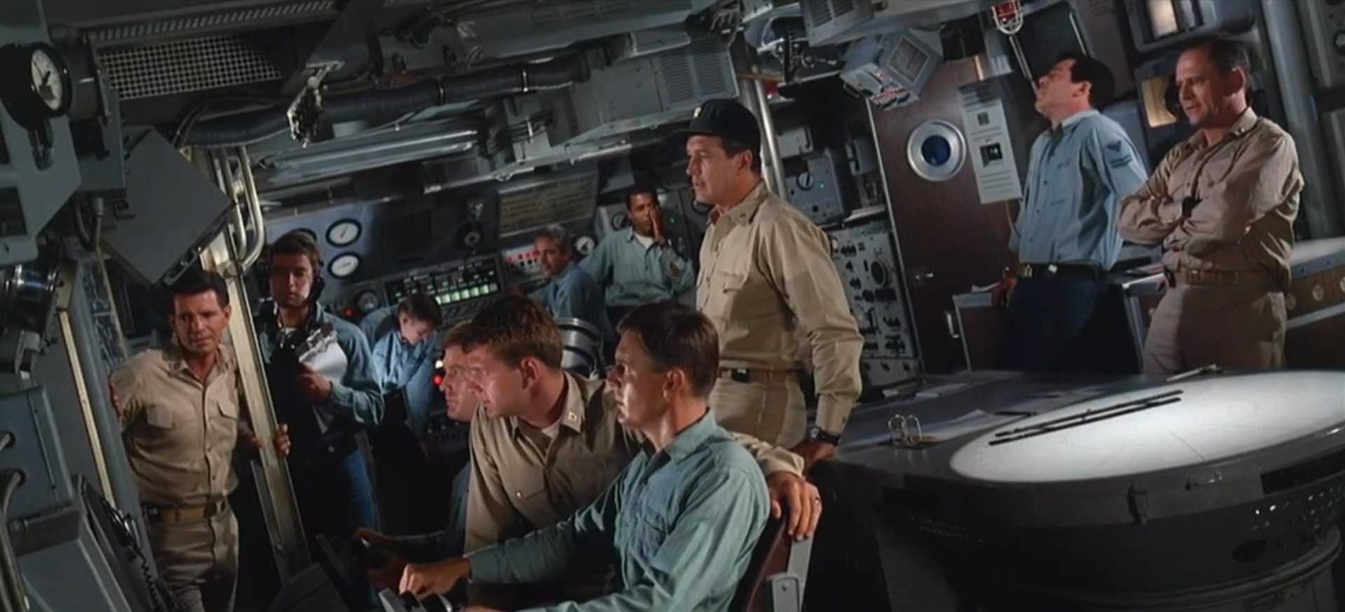 View of the command center of the US nuclear submarine, which is inclined to the left, with several crew members and Rock Hudson as commander in the center.
