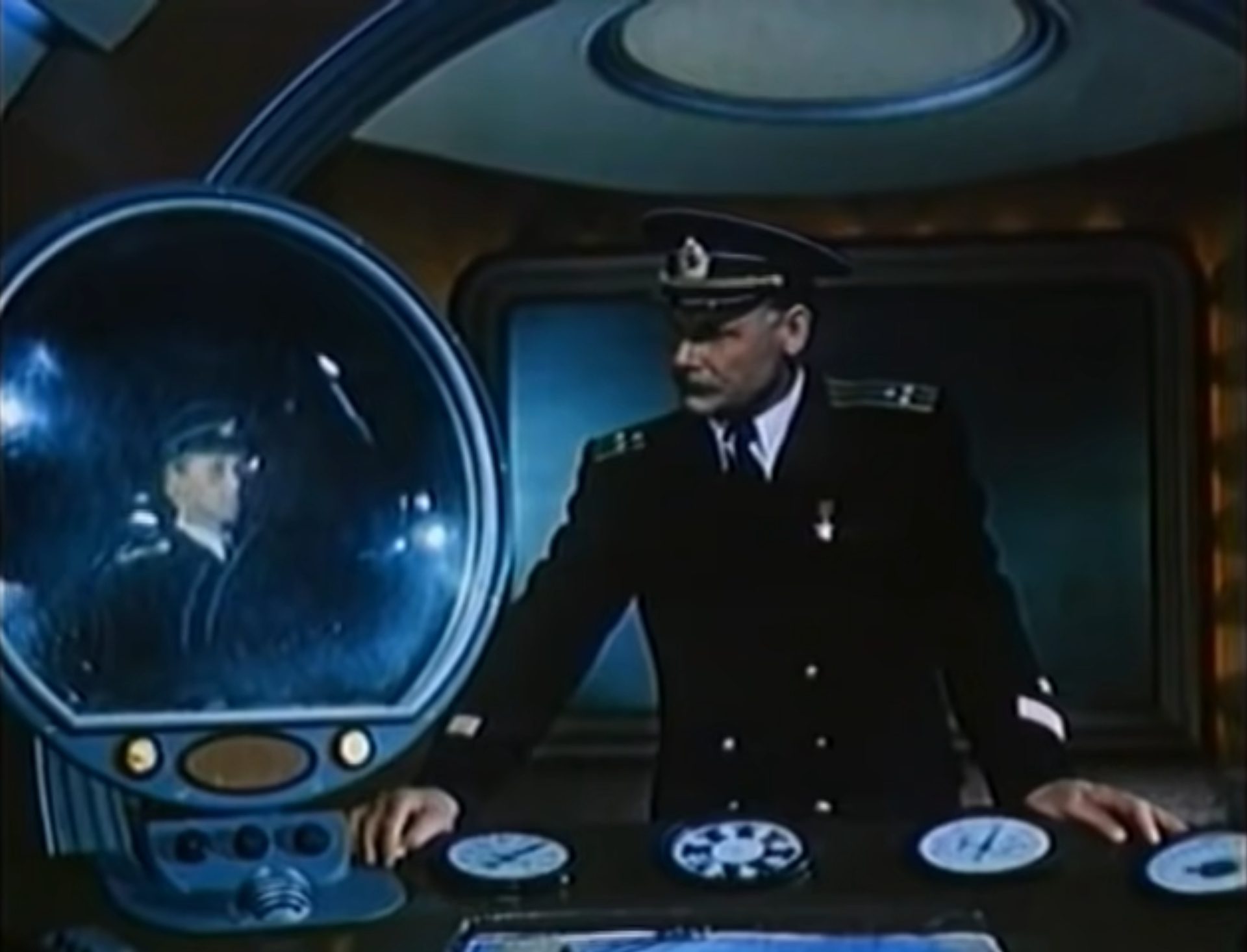 Uniformierter Kommandant lehnt an einem futuristischen Terminal und blickt auf einen Bildschirm, auf dem sich ein anderer Offizier abzeichnet.