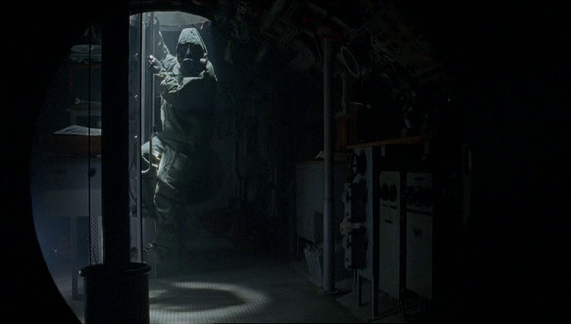 Im Lichtschein einer geöffneten Luke klettert ein Mann in Ganzkörperschutzkleidung eine Leiter hinab in das verlassene U-Boot.