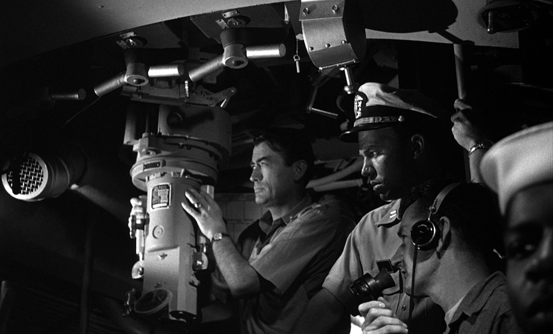 Oppressive black and white shot from the inside of the submarine, with Gregory Peck as commander in the presence of some sailors.