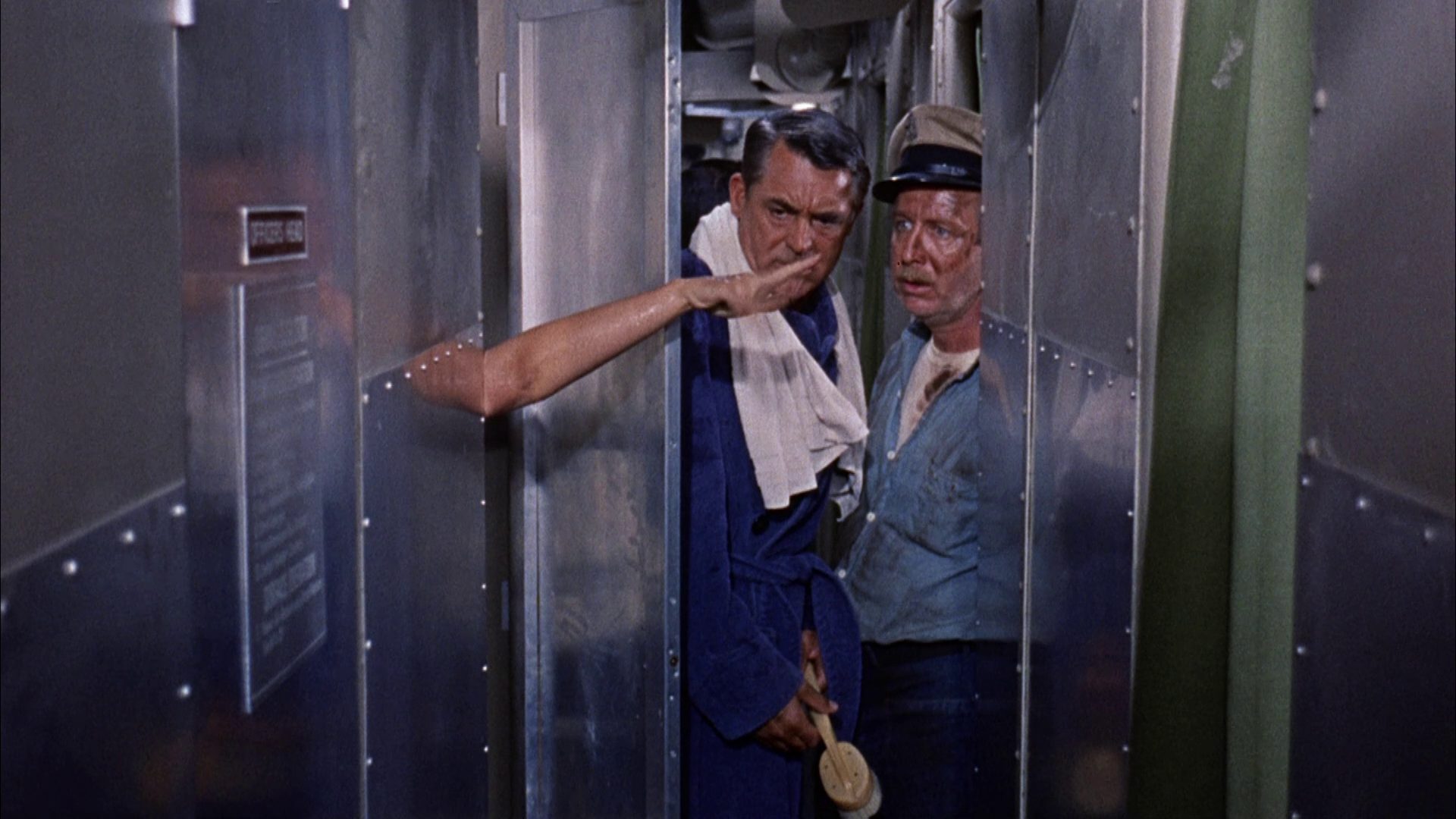 Cray Grant as a submarine captain in a bathrobe looks in the presence of one of his sailors in amazement at a woman's hand stretched out from the shower cubicle.