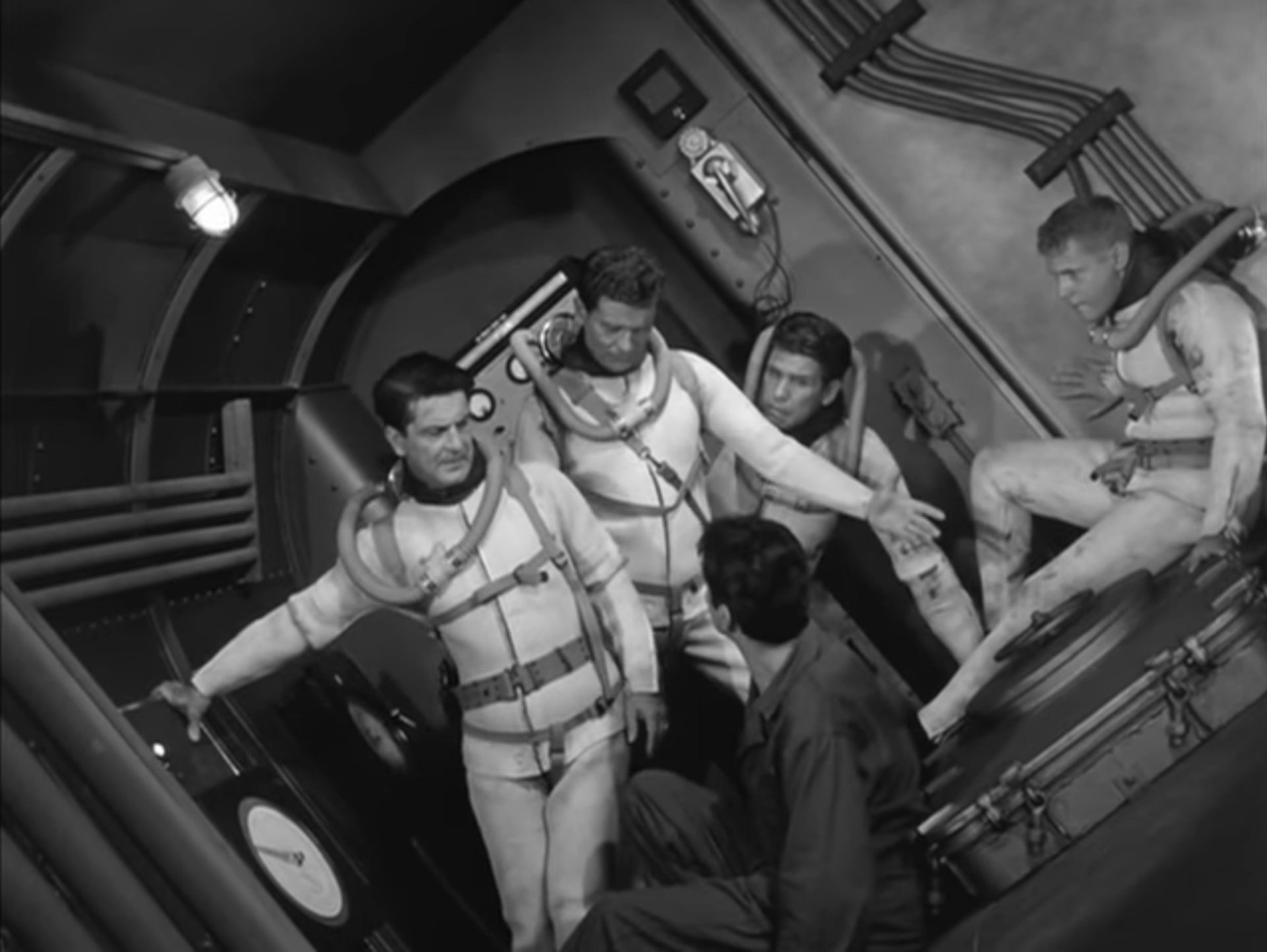 Schwarz-Weiß-Szene: Fünf Besatzungsmitglieder in Schräglage im U-Boot, vier von ihnen tragen Taucheranzüge ohne Helme.