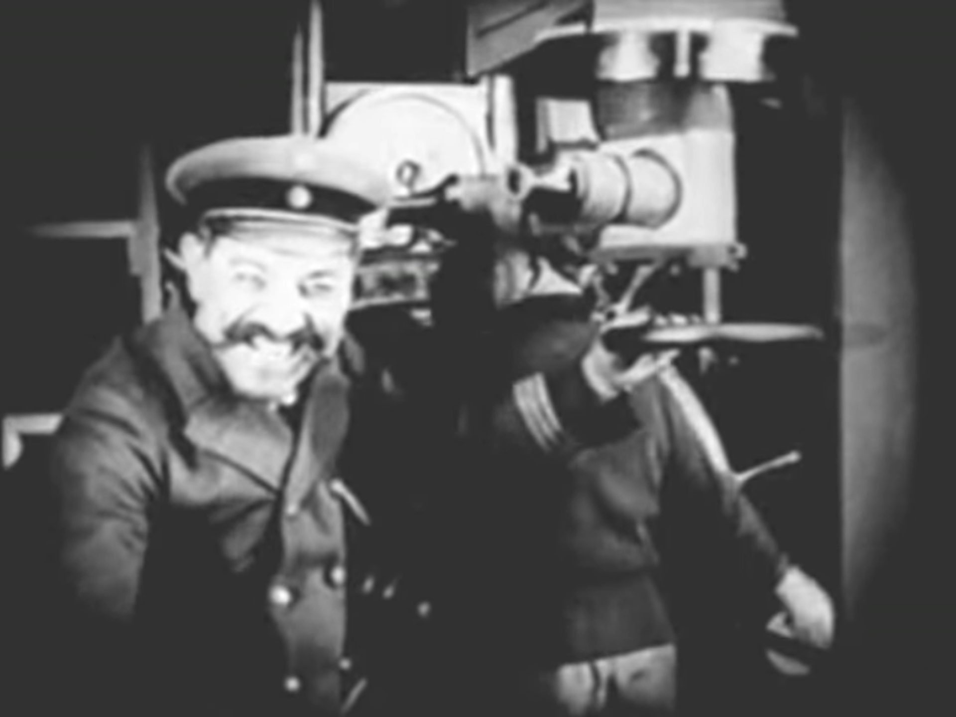 Schwarz-Weiß-Szene mit deutschem U-Boot-Kapitän, der mit einem fratzenhaften Grinsen am Periskop steht und zur Kamera blickt.