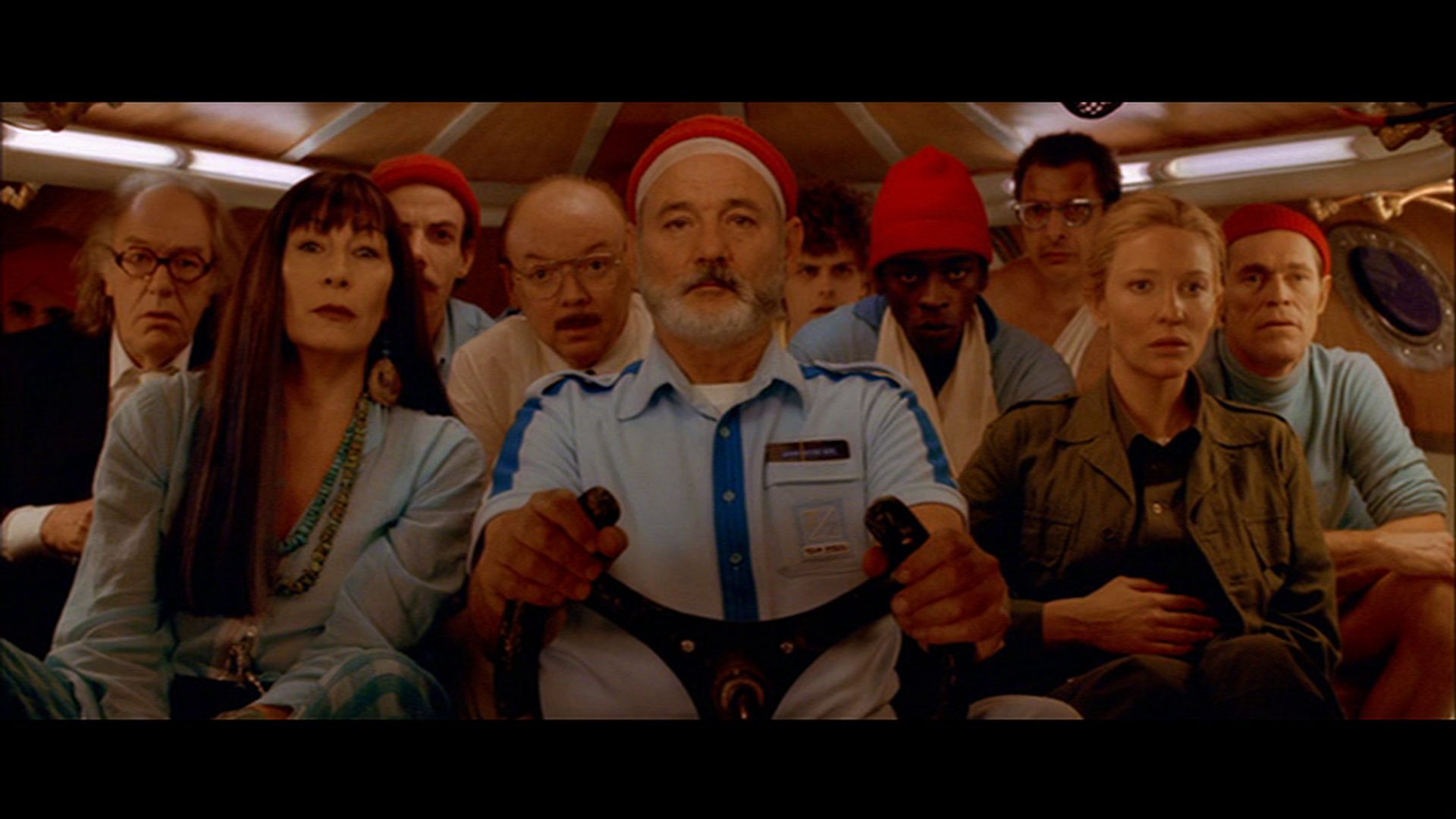 Frontalaufnahme von zehn Insassen eines Mini-U-Bootes mit konzentriert-gespannten Blicken, in der Mitte sitzt Bill Murray als Steve Zissou am Steuer, flankiert von Anjelica Huston und Cate Blanchett.