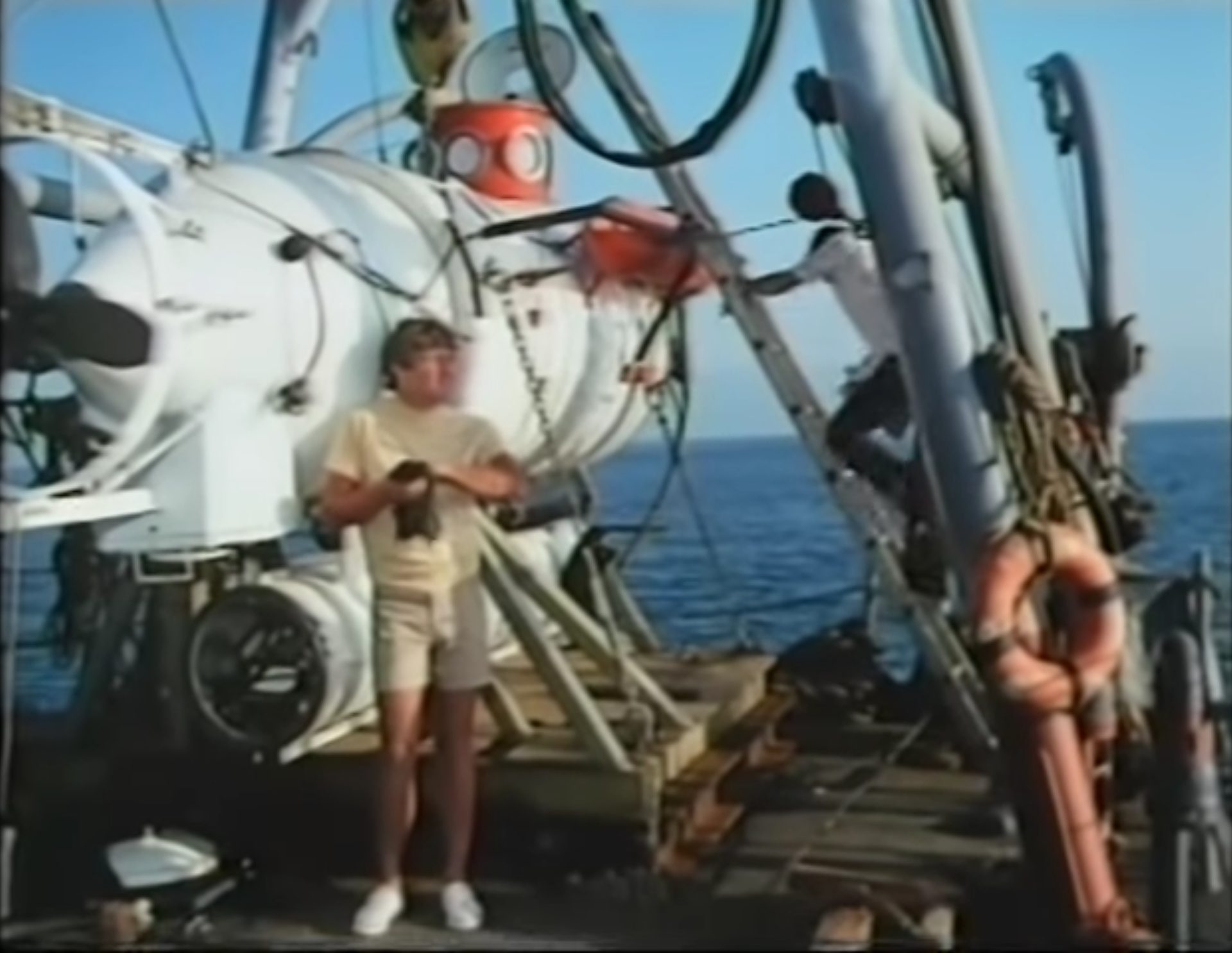 Weißes Mini-U-Boot an Deck eines Schiffes, zwei Männer bei Vorbereitungen.