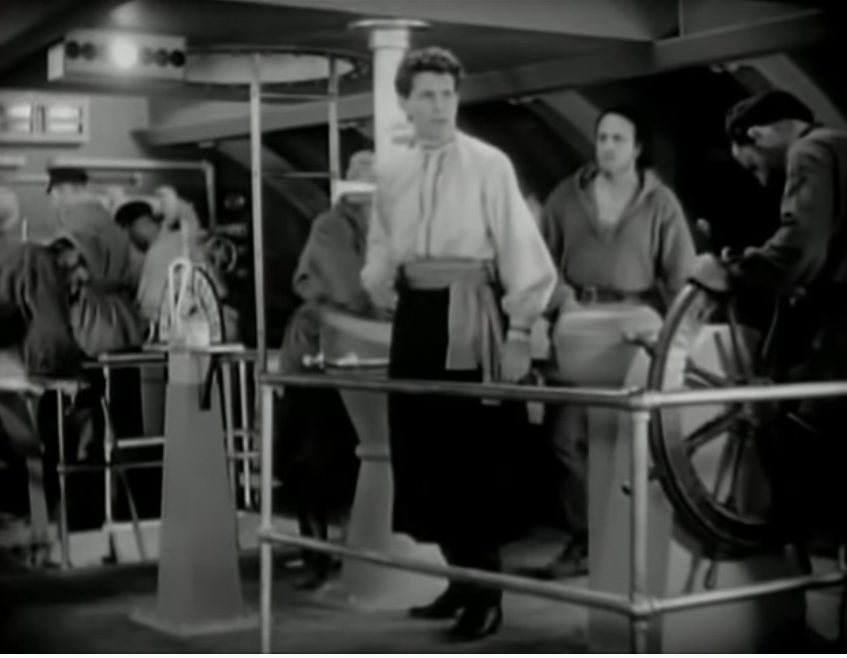 Schwarz-Weiß-Szene mit Blick in die U-Boot-Zentrale, in der eine geschäftige Crew ihren Dienst verrichtet.