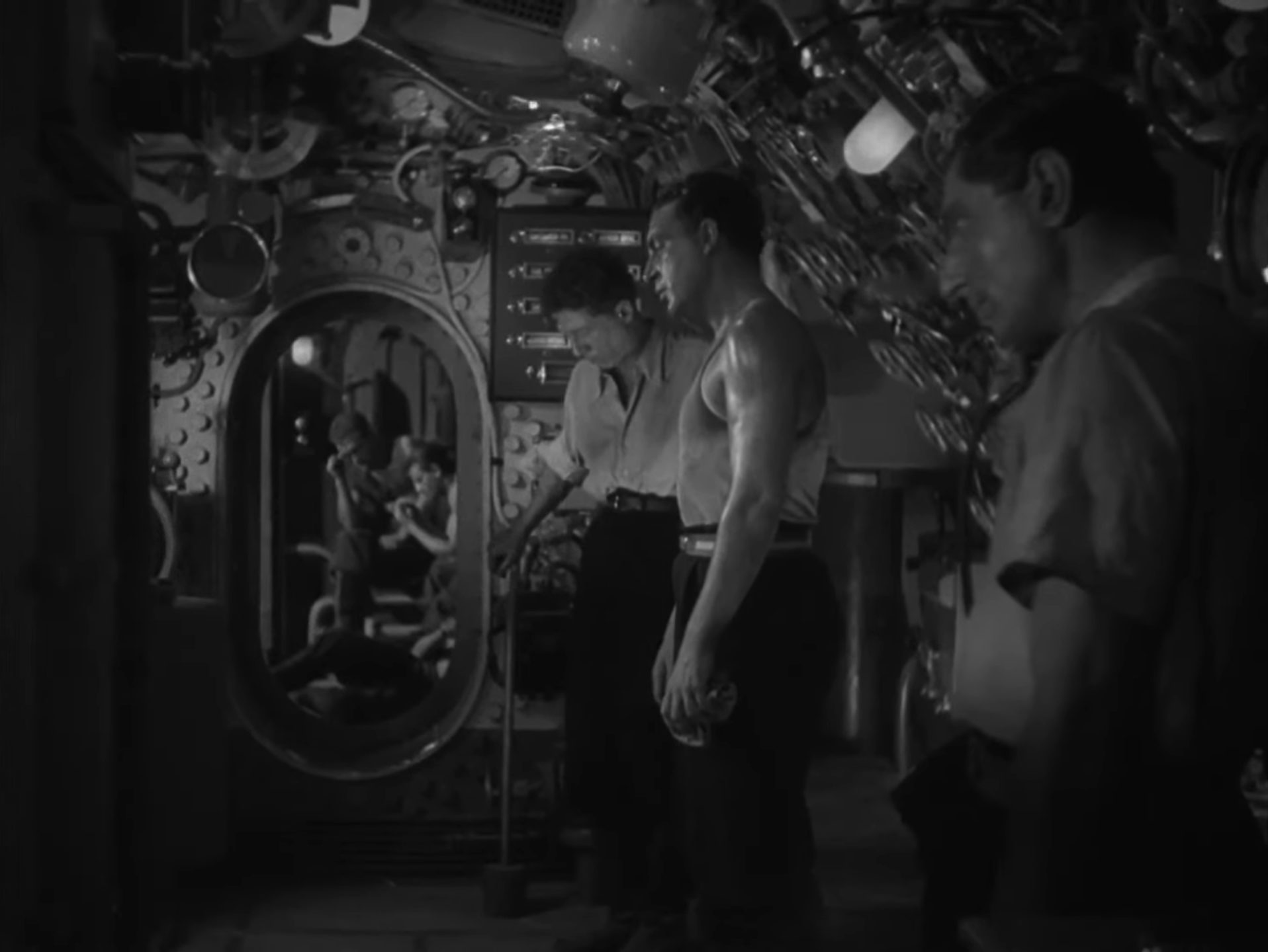 Schwarz-Weiß-Szene: Blick in die U-Boot-Zentrale und durch das Schott mit mehreren ermatteten Seeleuten.