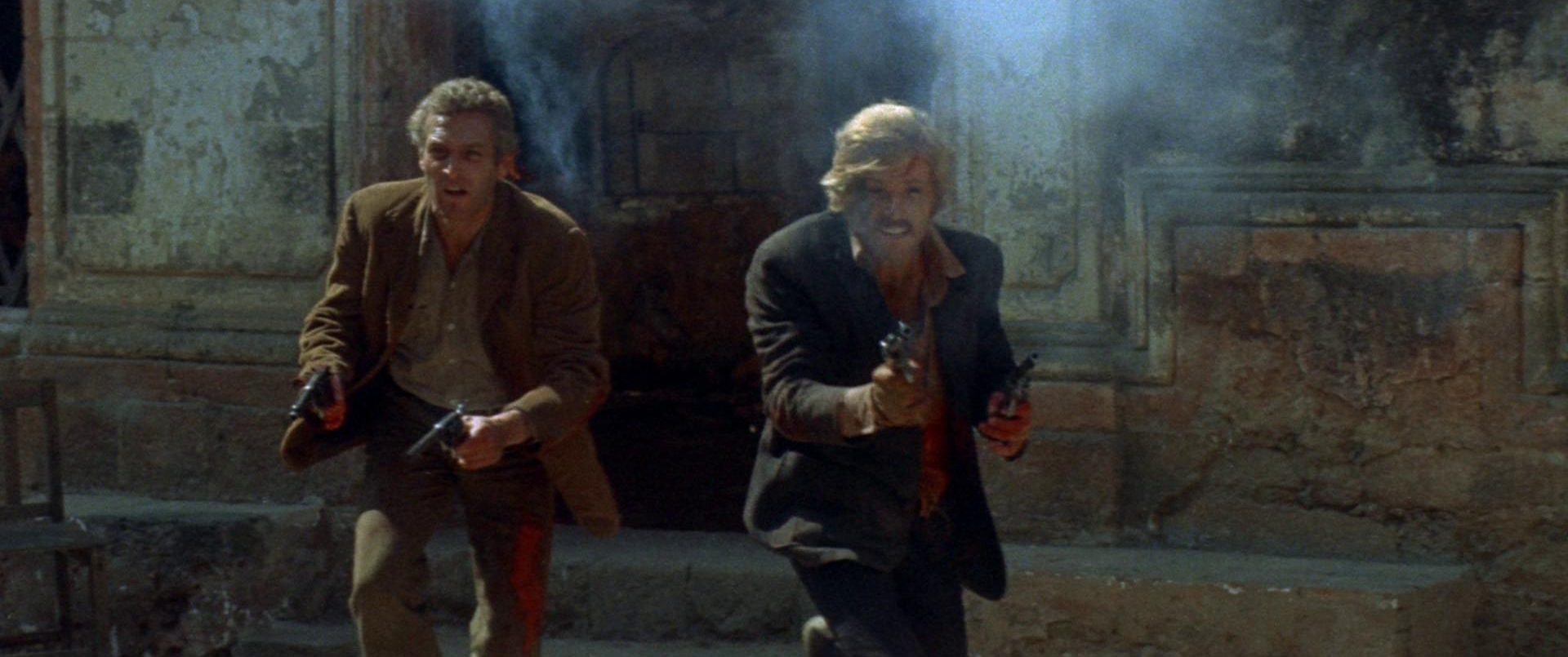 Paul Newman and Robert Redford as Butch Cassidy and the Sundance Kid with guns drawn in the middle of a shootout.