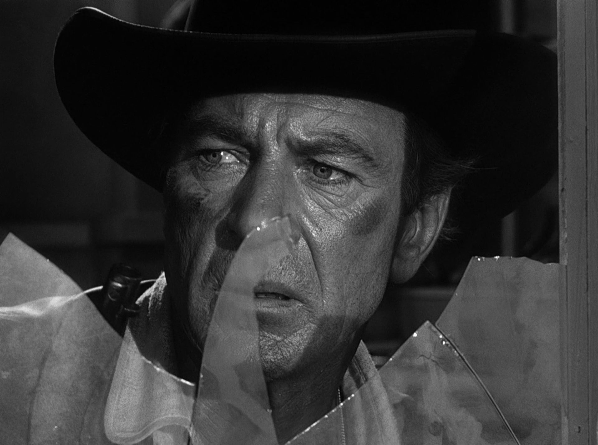 Close-up of Gary Cooper as Marshal Will Kane with frightened-skeptical face behind a shattered window pane.