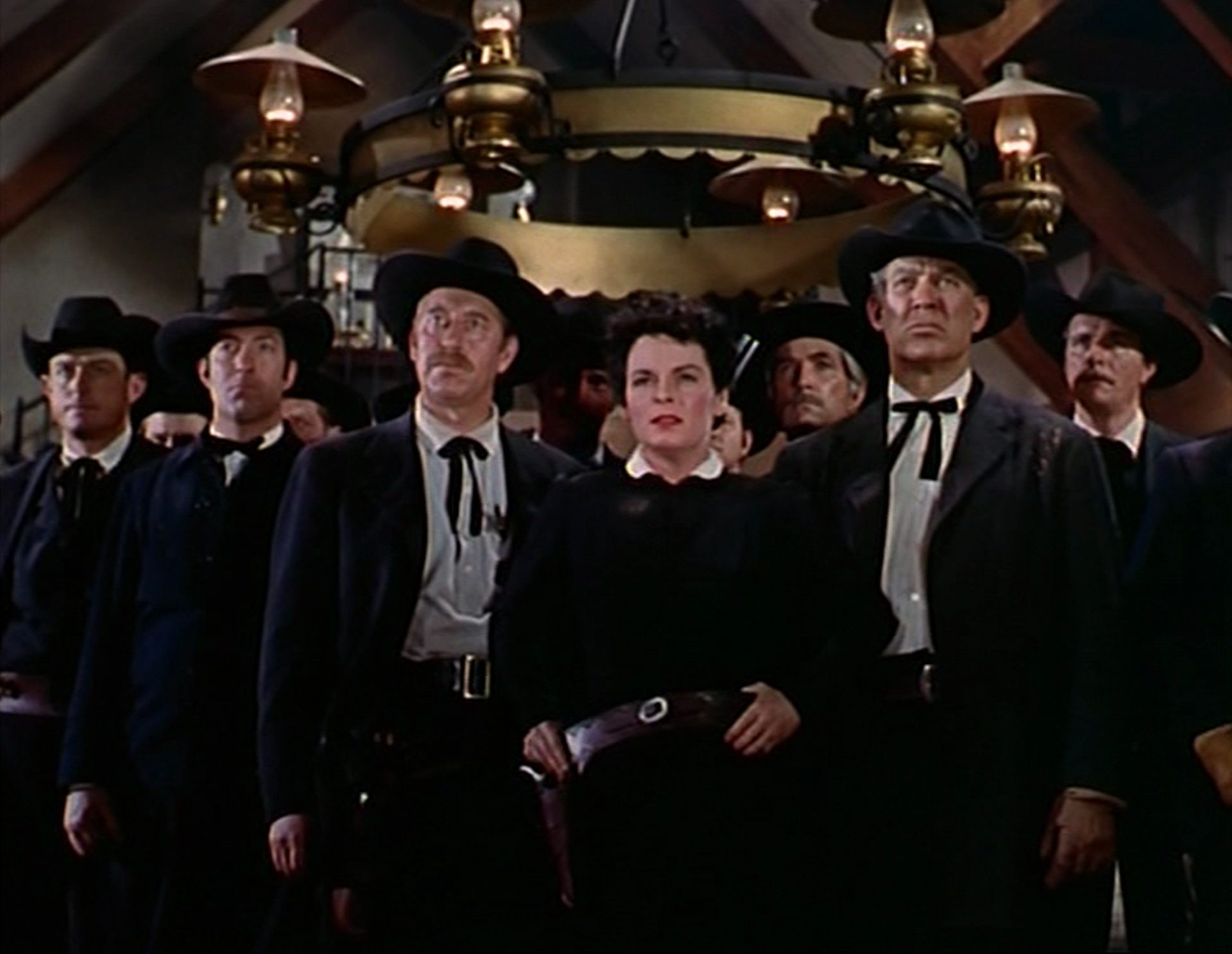 Mercedes McCambridge as Emma Small in a militant pose at the head of an otherwise all-male group under a chandelier.
