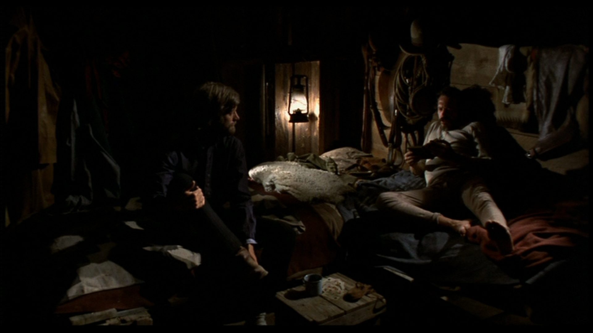 Harry Collings and Arch Harris go to bed in a sparsely lit cabin.