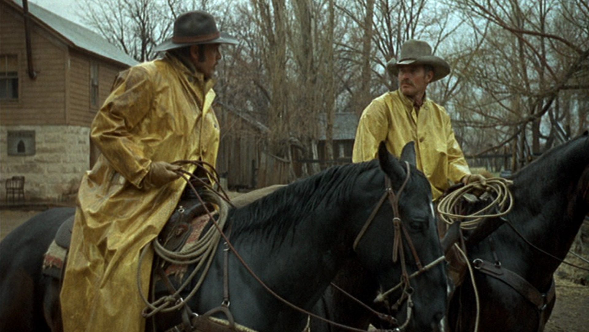 Will Penny talking to a ranch hand on horseback in rain jackets.