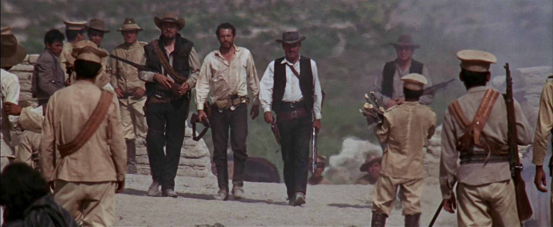 Die Banditen marschieren bewaffnet durch einen mexikanischen Ort.
