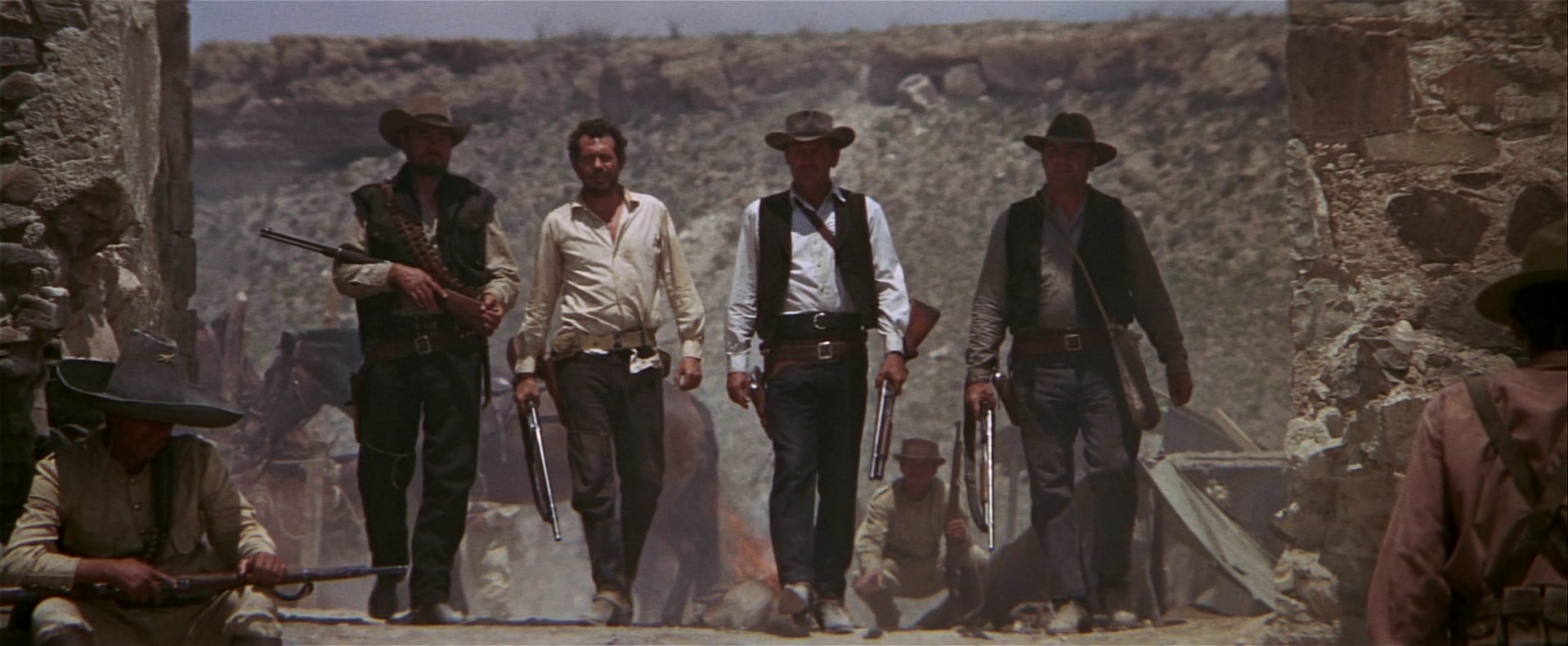 Ben Johnson, Warren Oates, William Holden und Ernest Borgnine marschieren nebeneinander als bewaffnete Outlaws im Lager der mexikanischen Soldaten.