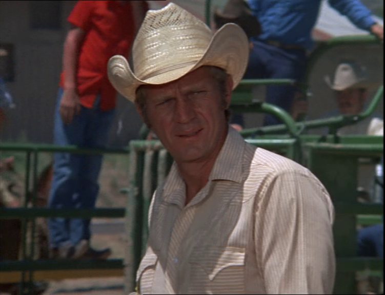 Close-up of Steve McQueen as ex-rodeo champion Junior Bonner, with a stoic, strained look.