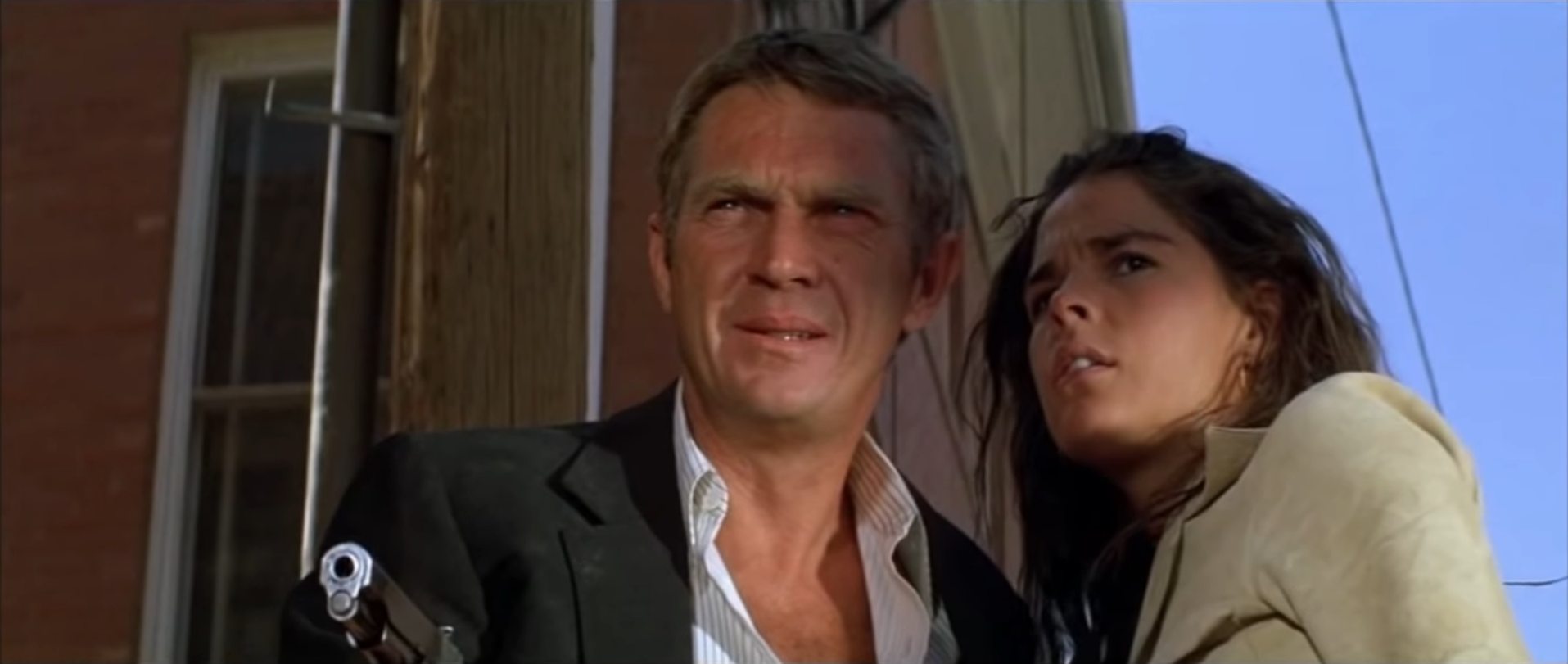 Close-up of Steve McQueen and Ali MacGraw as gangster couple in alerter pose; he holds a gun at the ready.