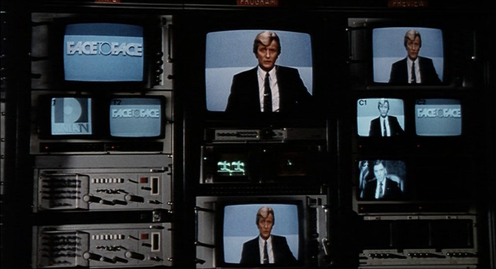 Rutger Hauer as a television journalist, shown on several monitors in a TV studio.