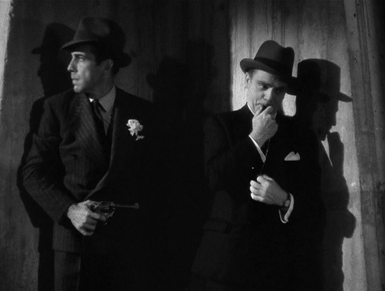 Schwarz-Weiß-Szene mit Humphrey Bogart und James Cagney als Prohibitionsganoven im Anzug mit Hut in einer dunklen Nische, Bogarts Charakter trägt einen Revolver.