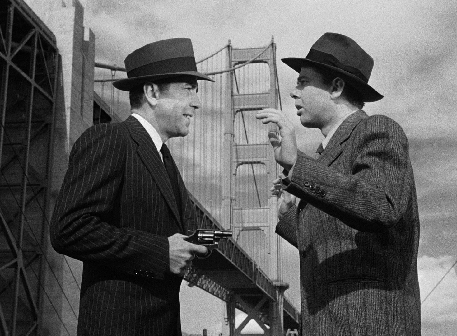 Black-and-white scene with Humphrey Bogart as Vincent Parry threatening a man, played by Clifton Young, with a revolver against the backdrop of the Golden Gate Bridge.