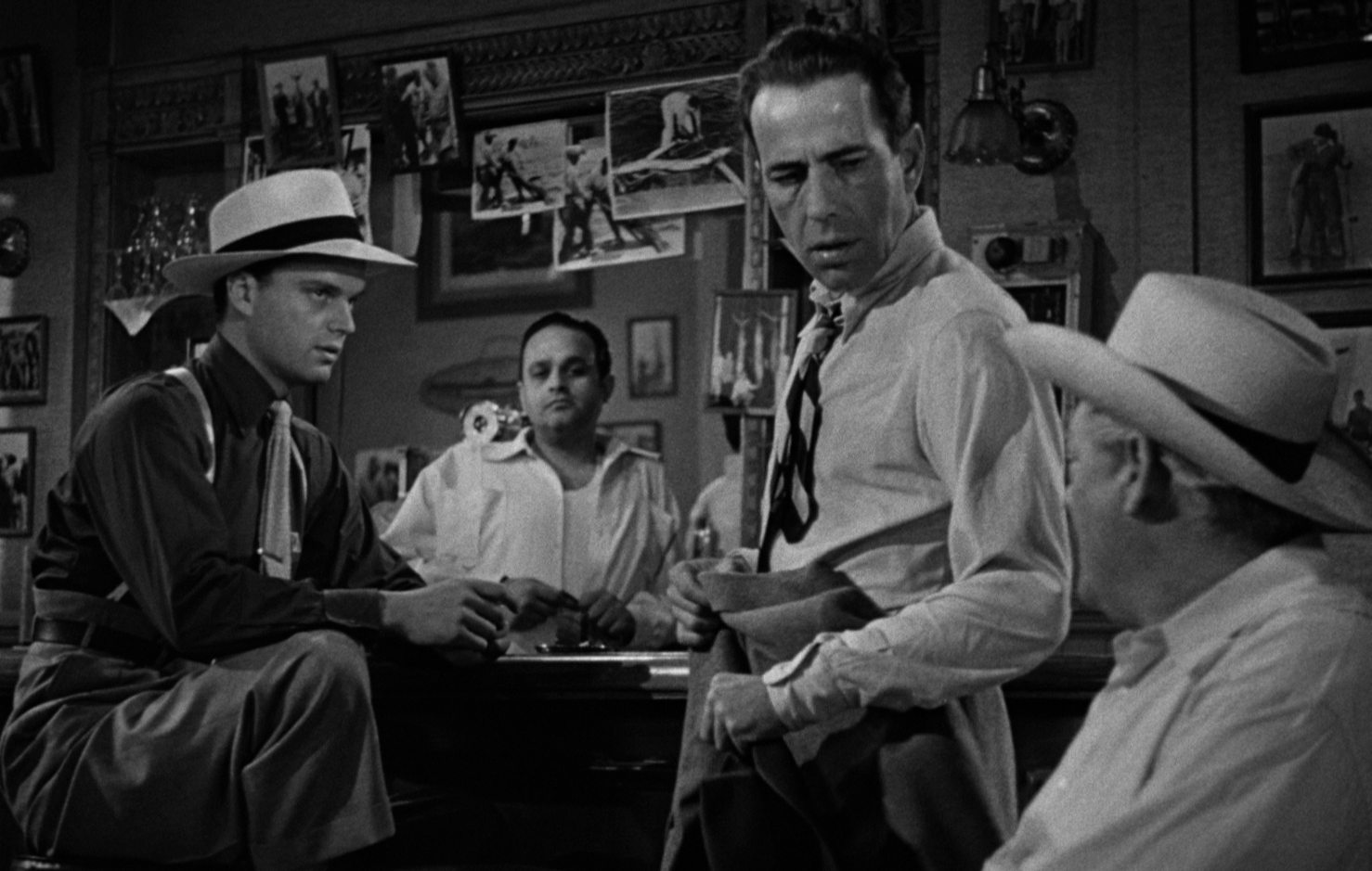 Black and white scene in which Humphrey Bogart turns to the owner at the edge of the picture in the hotel, in the presence of two crooks.