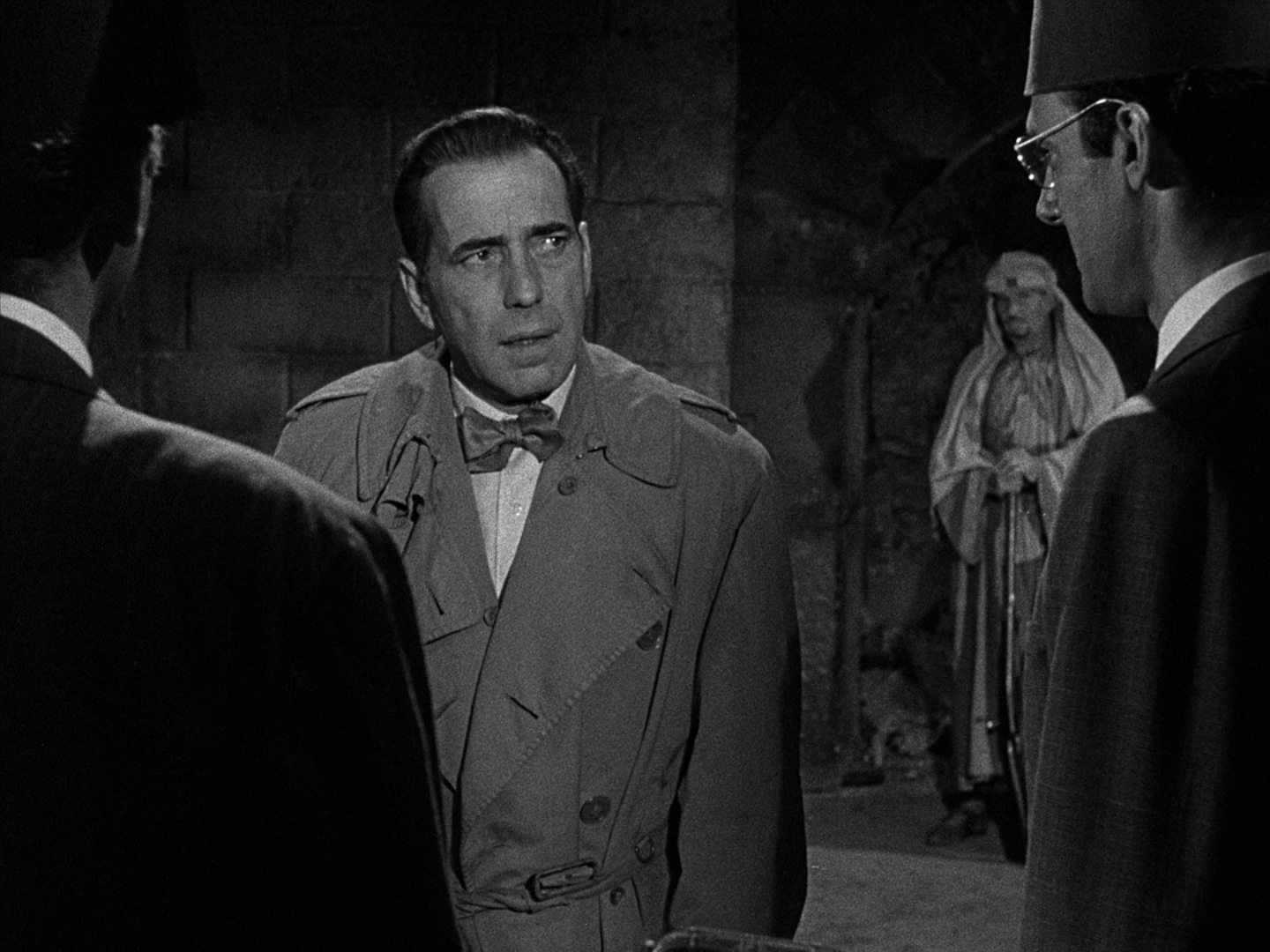 Schwarz-Weiß-Szene mit Humphrey Bogart als Schmuggler in dubioser Umgebung im Gespräch. 