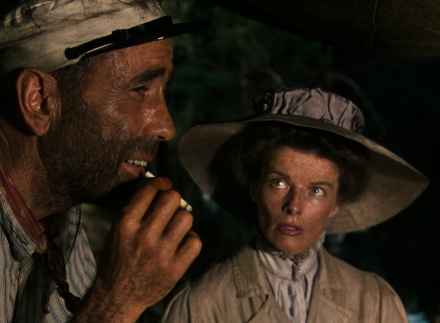 Humphrey Bogart mit Vollbart und Zigarette als abgekämpfter Bootskapitän, Katharine Hepburn in vornehmer Haltung blickt zu ihm auf.