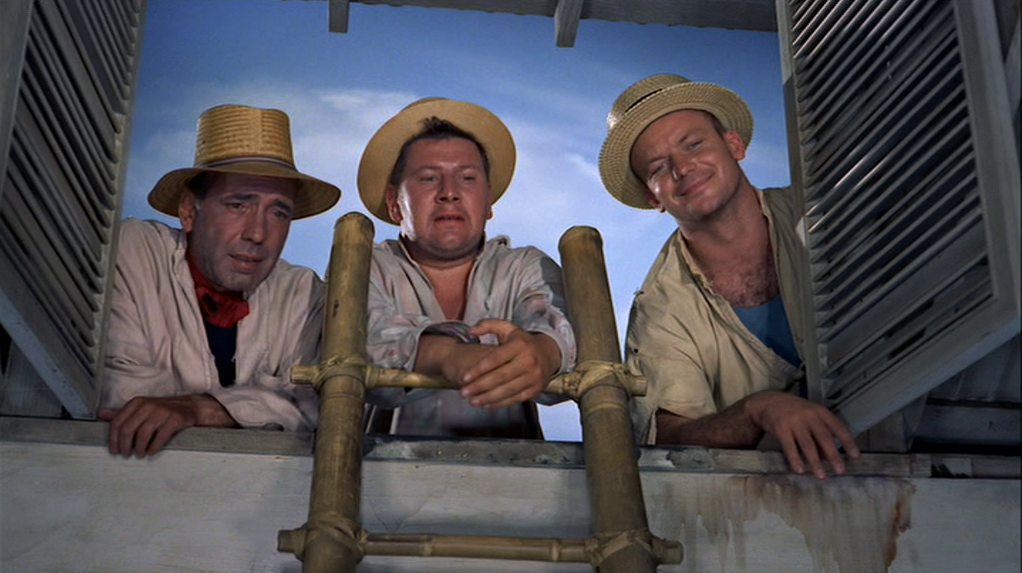 Humphrey Bogart, Peter Ustinov and Aldo Ray peer out of an open skylight into a house; all three ragged inmates are wearing new woven hats.