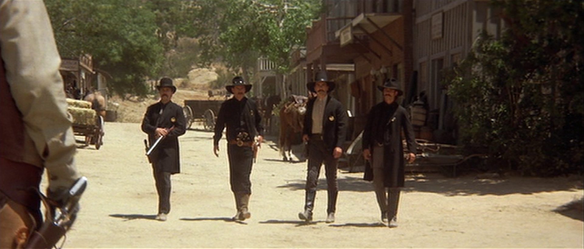 Blick auf vier schwarz gekleidete Männer mitten auf der staubigen Hauptstraße einer Westernkleinstadt.
