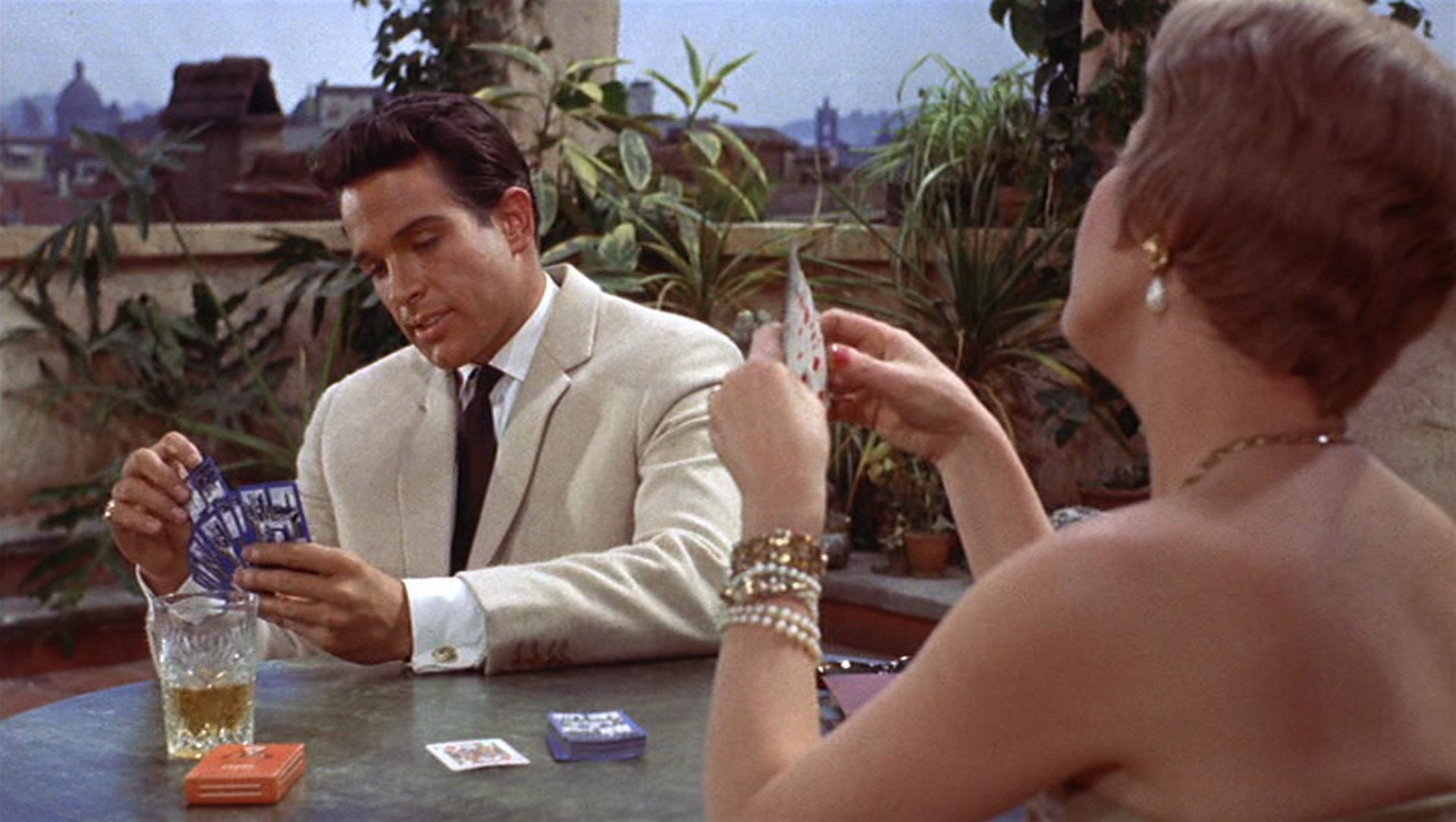 Italienisches Dolce-Vita-Flair: Warren Beatty im hellen Anzug beim Kartenspiel am Tisch mit einer ihm gegenüber sitzenden Frau.
