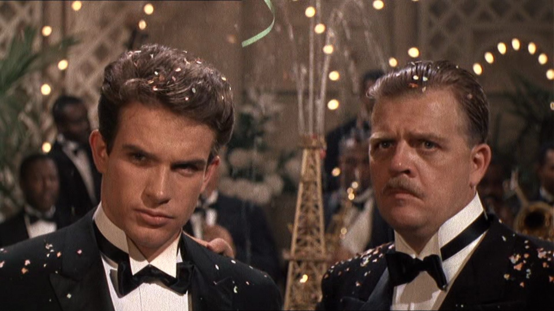 Nahaufnahme von Warren Beatty und Pat Hingle mit skeptischen Blicken in Abendgarderobe bei einer großen Feier, Konfetti auf den Schultern.