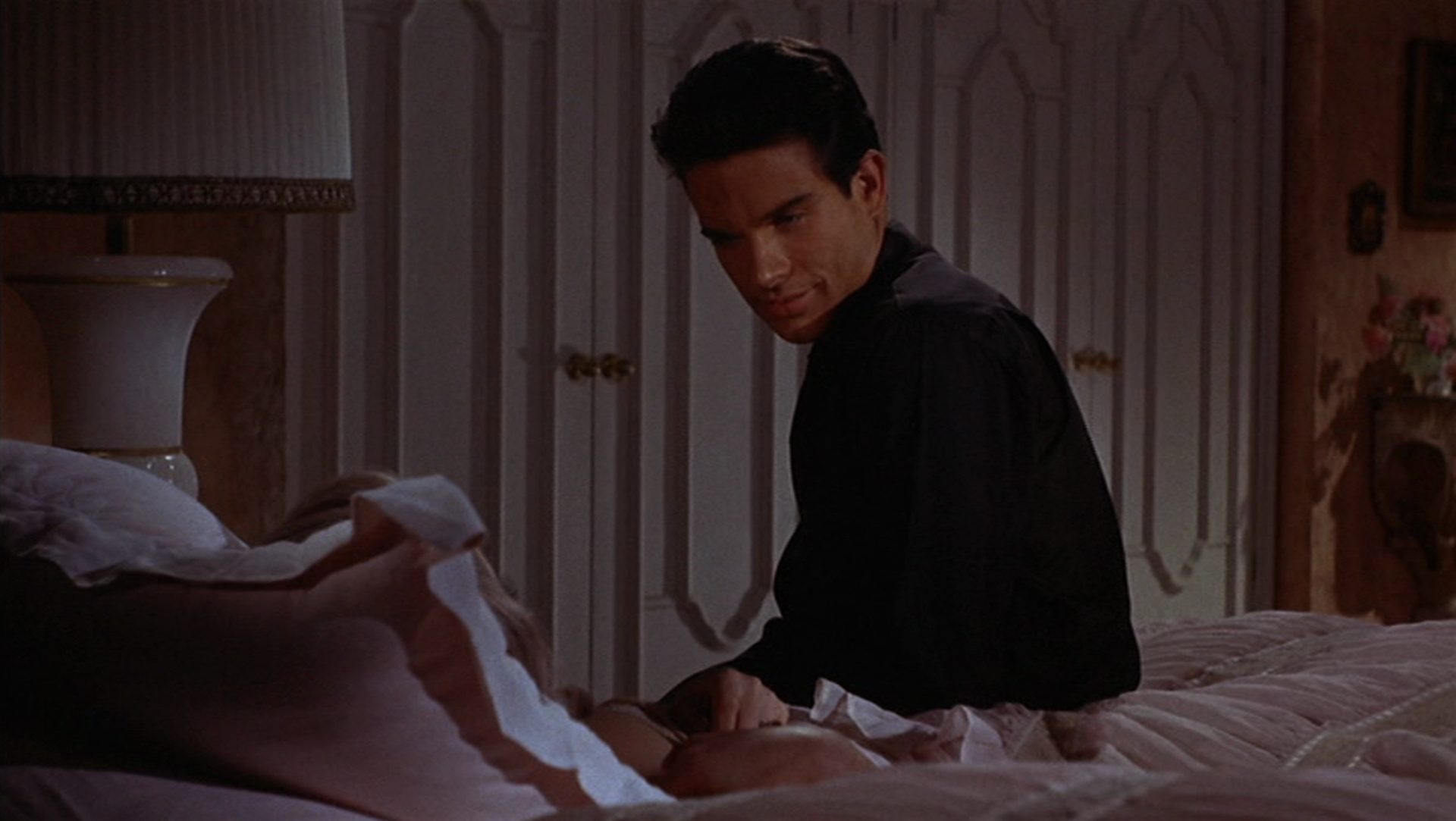 Warren Beatty sitzt in einem schwach beleuchteten Zimmer auf dem Bett, hinter dem Kissen erkennt man eine Frau.