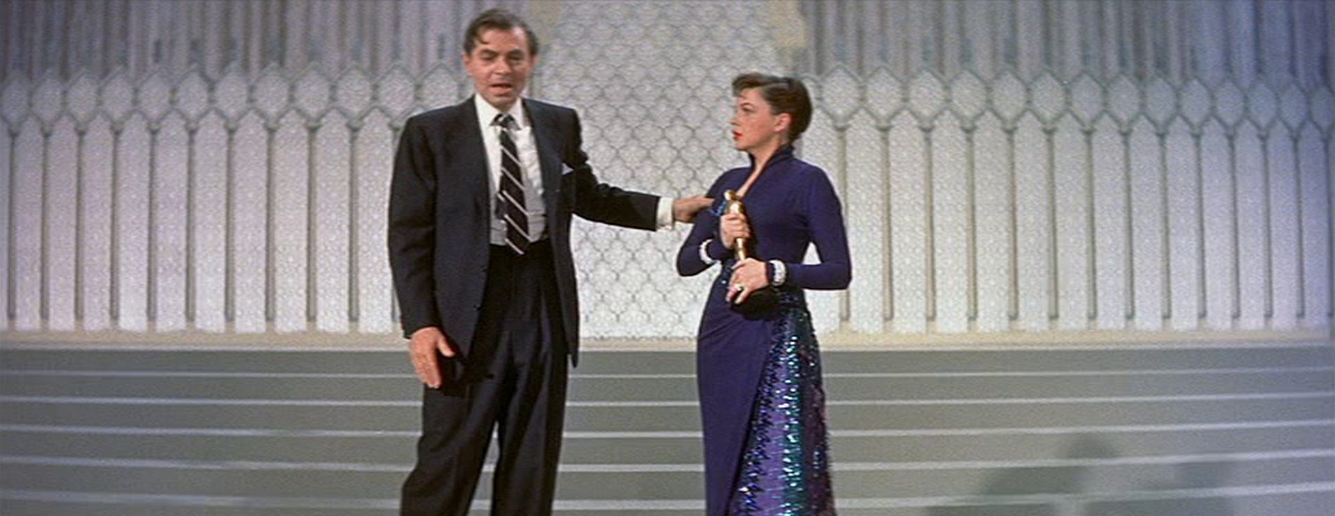 James Mason als Ex-Hollywoodstar Norman Maine betrunken auf der glamourösen Bühne der Academy Awards im Beisein seiner just oscarprämierten Ehefrau Esther Blodgett, gespielt von Judy Garland.