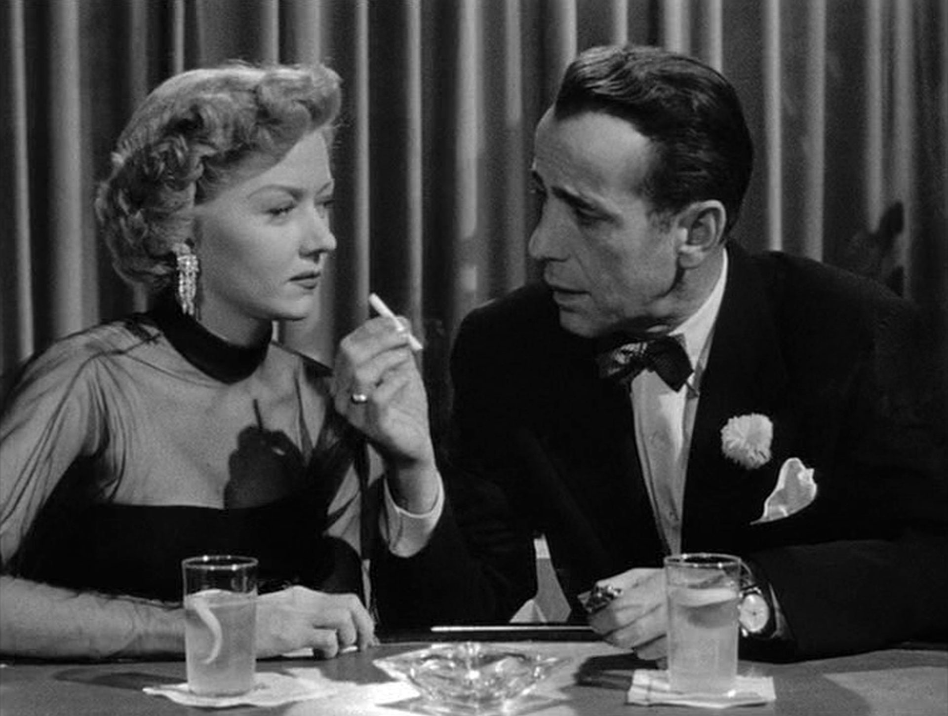 Gloria Grahame als Laurel Gray, die sich mit skeptischem Gesichtsausdruck in einer Bar von dem Drehbuchautor Dixon Steele, gespielt von Humphrey Bogart, eine Zigarette reichen lässt.