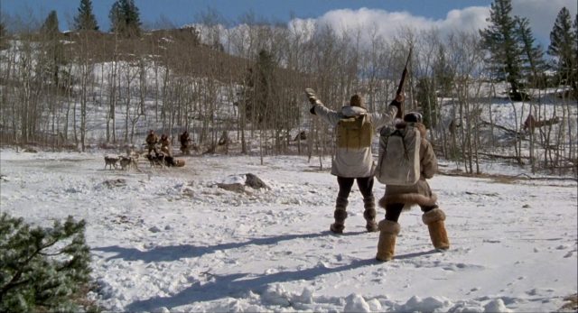 Millen signalisiert inmitten der Schneelandschaft mit seinen Armen in Richtung einer mit Schlitten herannahenden Gruppe.