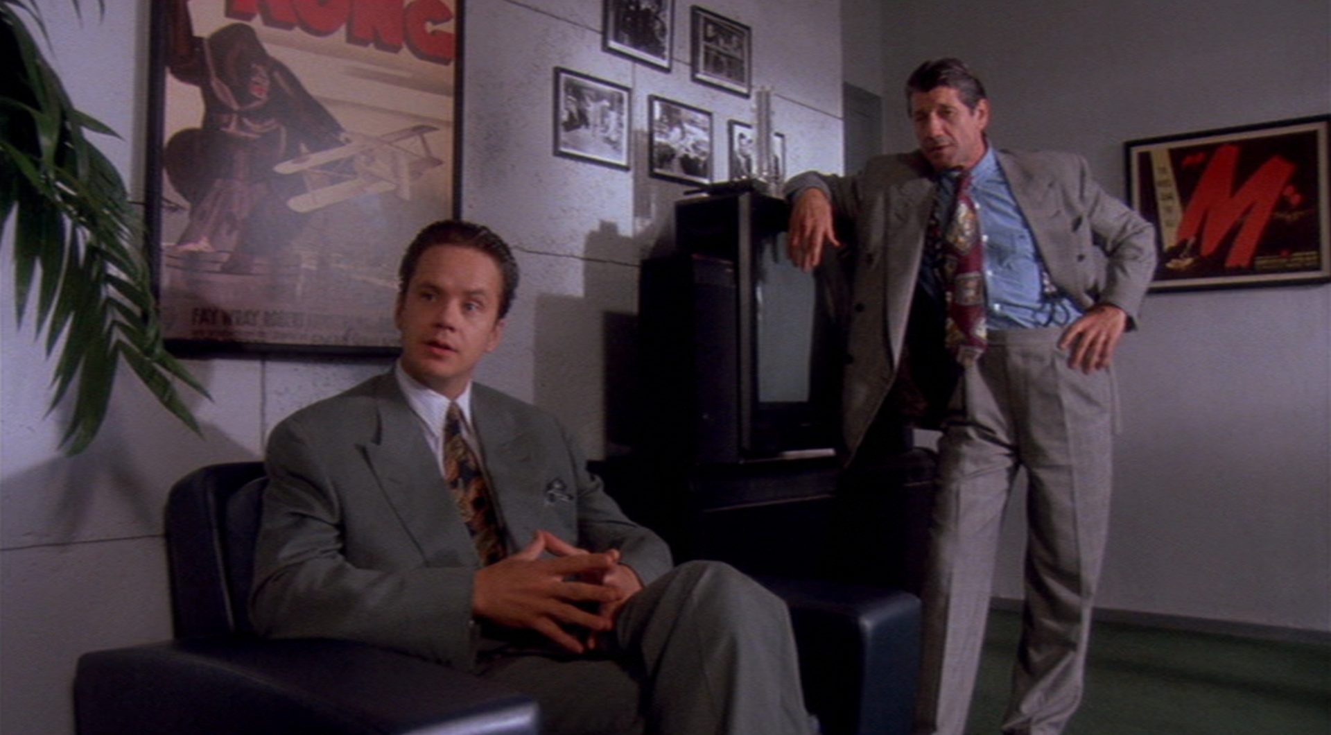 Griffin Mill sitzt in gespielter Gelassenheit in seinem Büro, hinter ihm ein klassisches „King Kong“-Filmplakat, neben ihm steht der Troubleshooter des Studios, gespielt von Fred Ward, an einen Röhrenfernseher gelehnt.