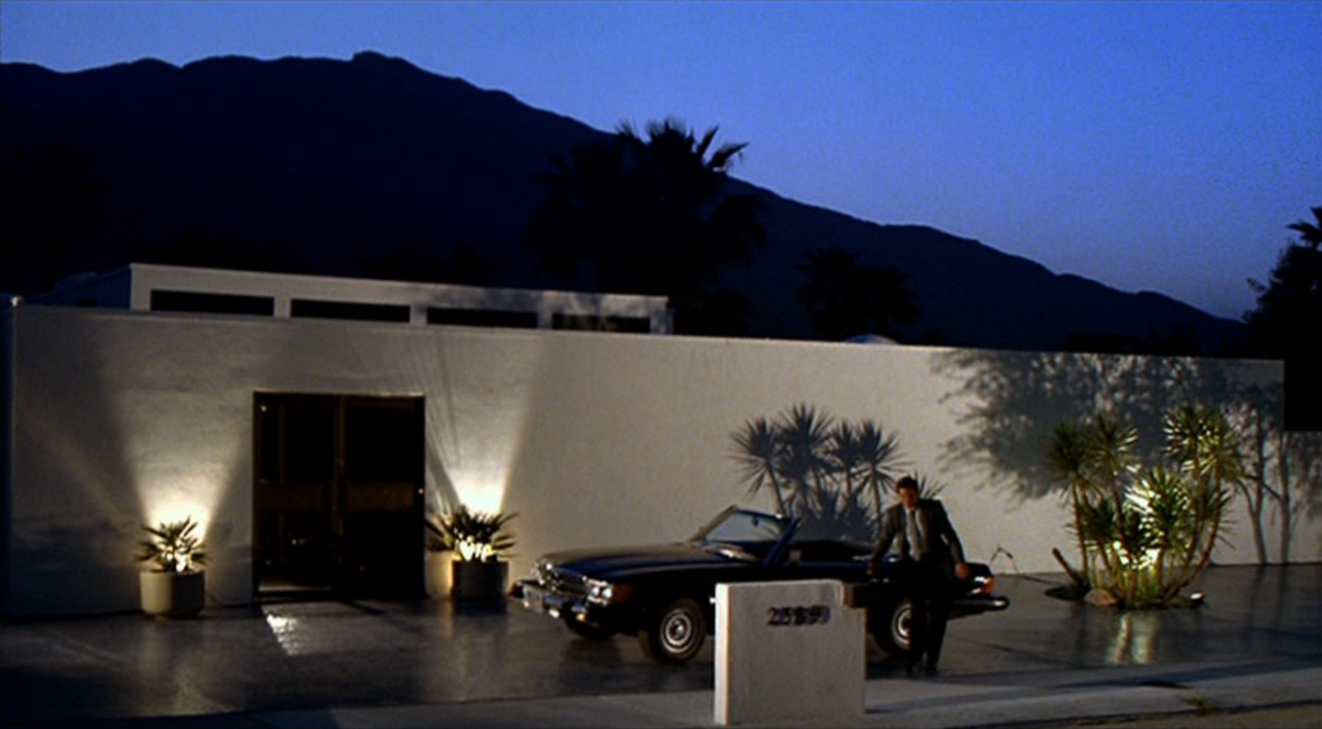 Kaye entsteigt in kalifornischer Abendatmosphäre seinem Cabriolet vor einem Luxusbungalow.