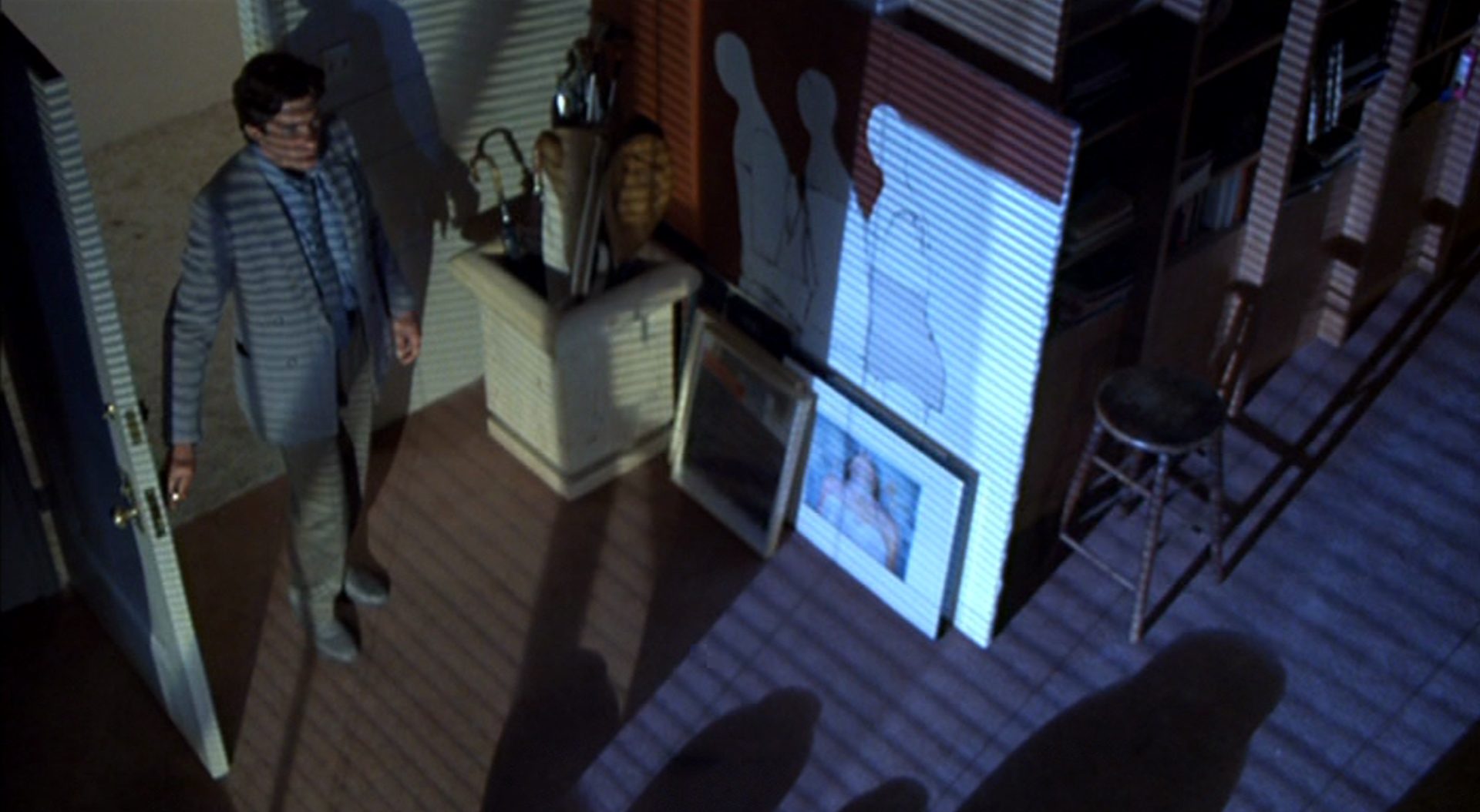 Blick von der Zimmerdecke auf Julian Kaye, auf dem der Lamellenschatten der Jalousie liegt.